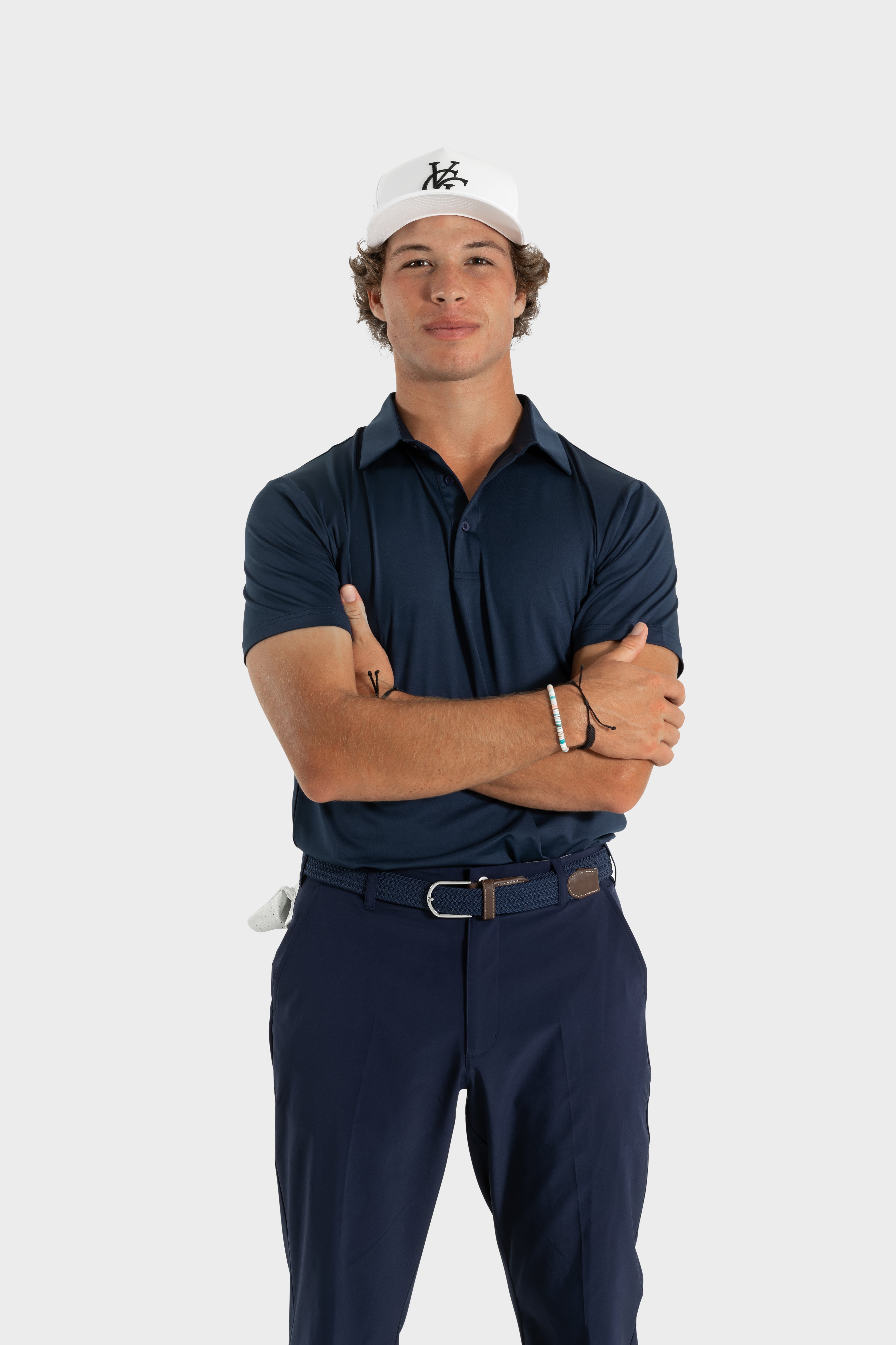 Man wearing The Abyss Golf Polo navy blue breathable tailored fit golf shirt and matching pants with a white golf cap