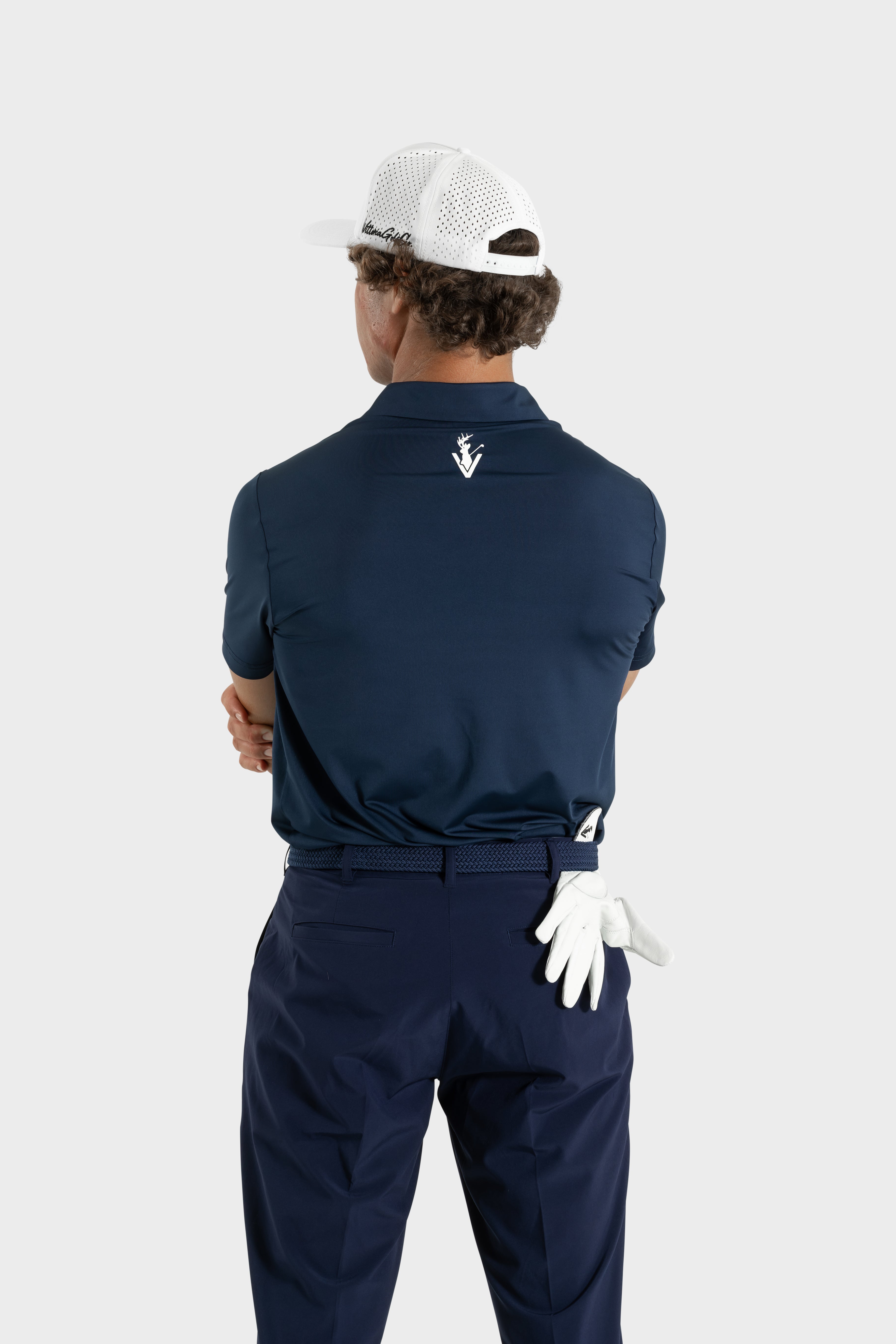 Man wearing navy The Abyss Golf Polo from behind with white cap and golf glove in pocket