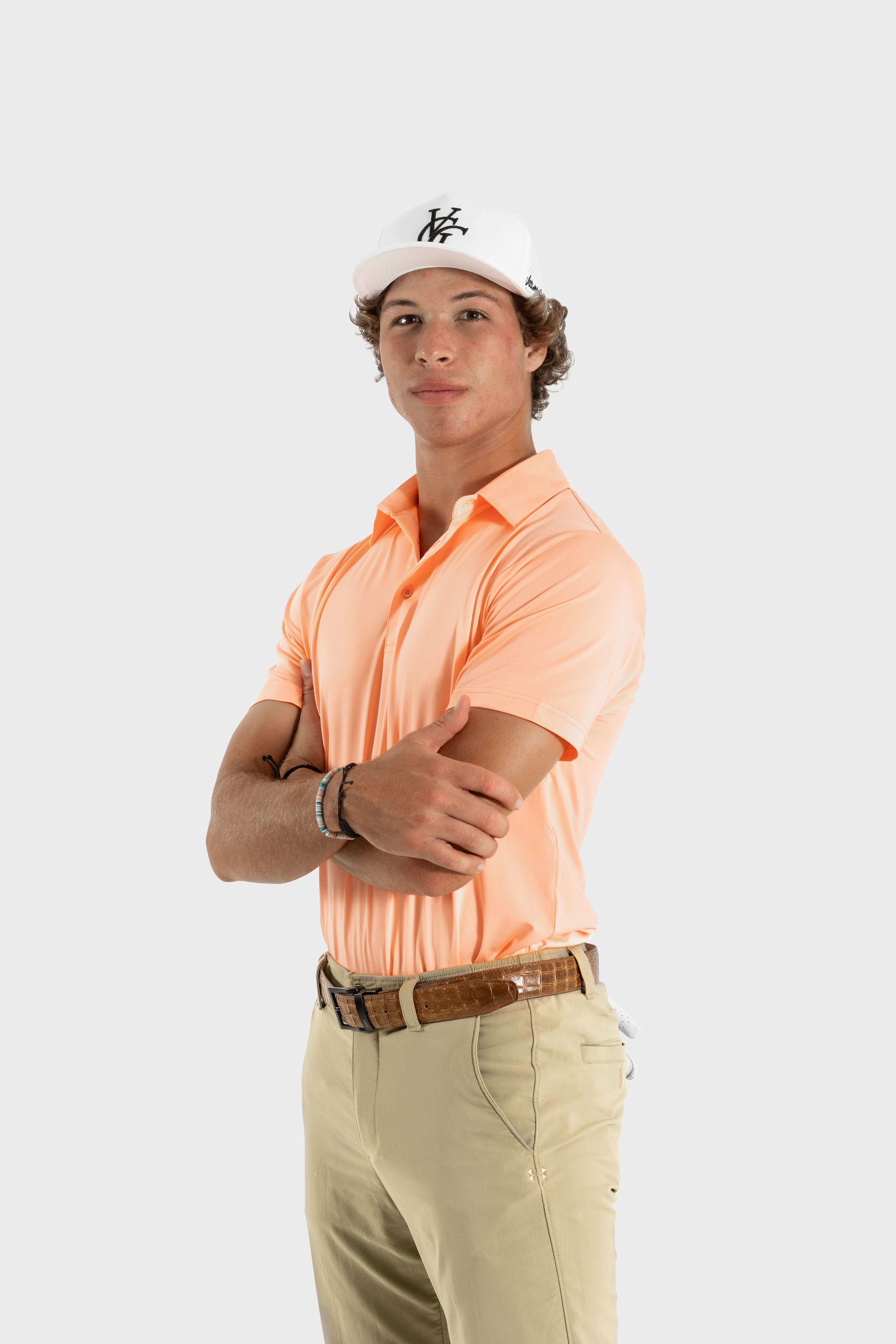Male model wearing peach The Dawn Golf Polo and beige pants with white cap