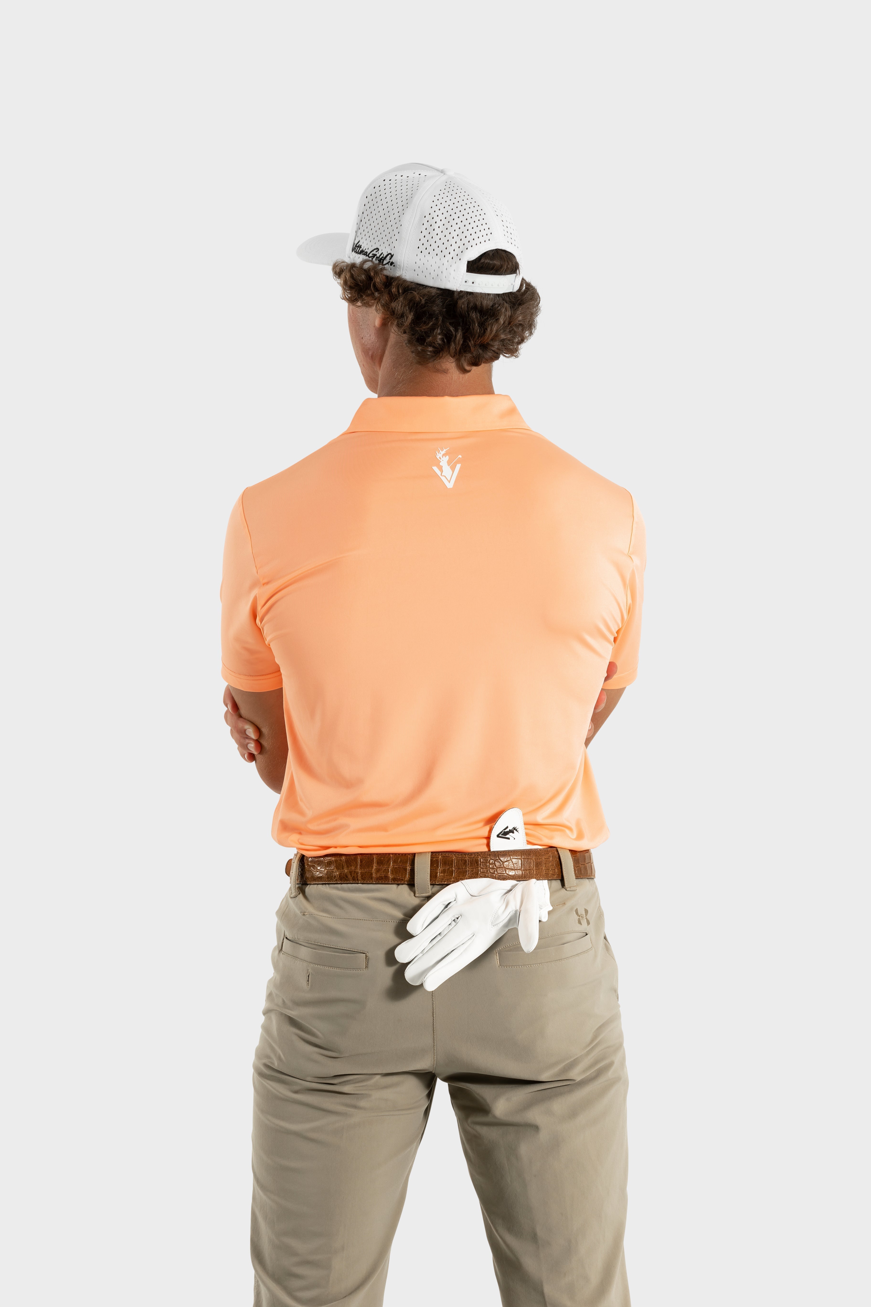 Man wearing The Dawn Golf Polo peach shirt and white cap, back view with golf glove tucked in belt loop