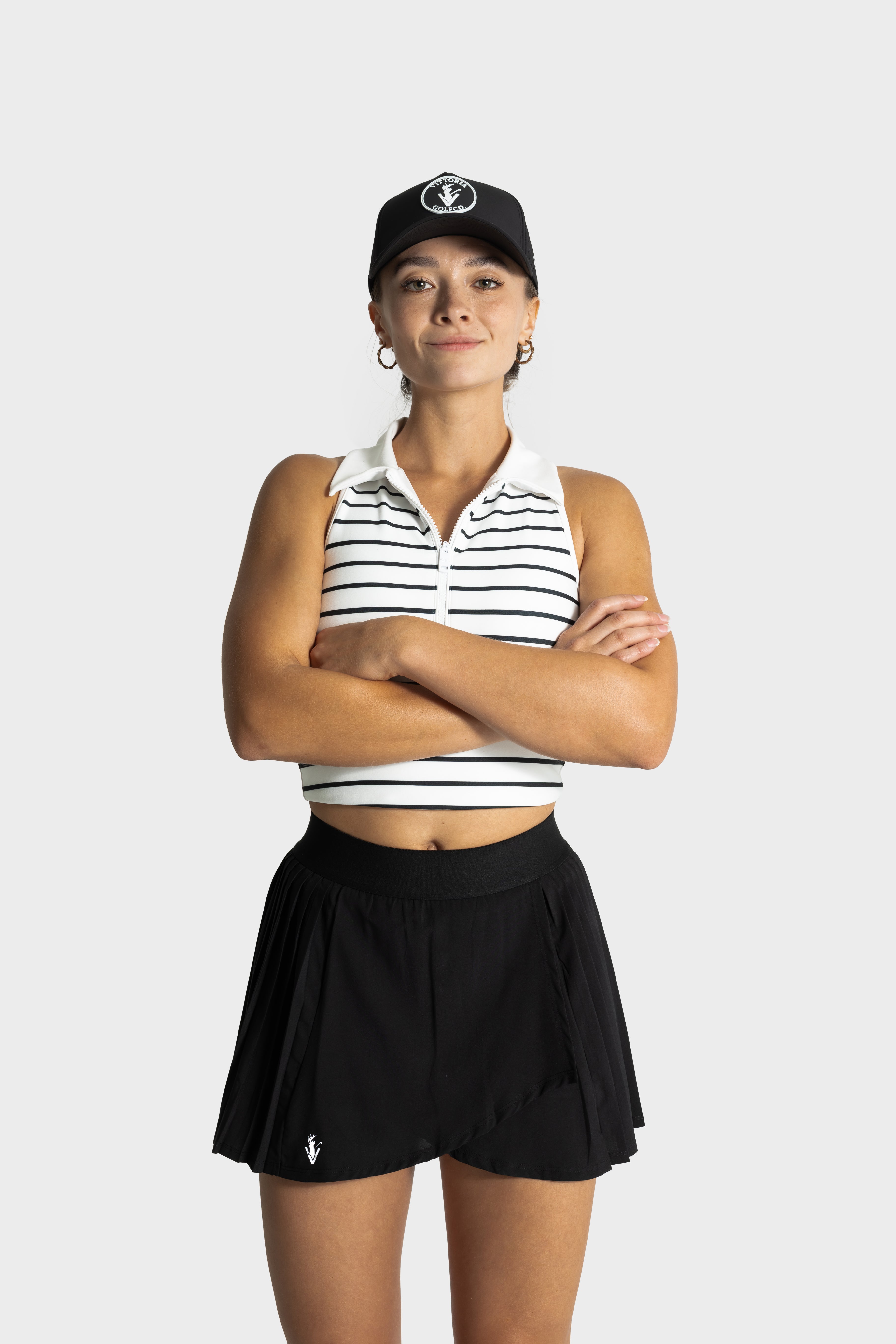 Woman wearing black Perfetta golf skirt and striped sleeveless polo shirt with cap