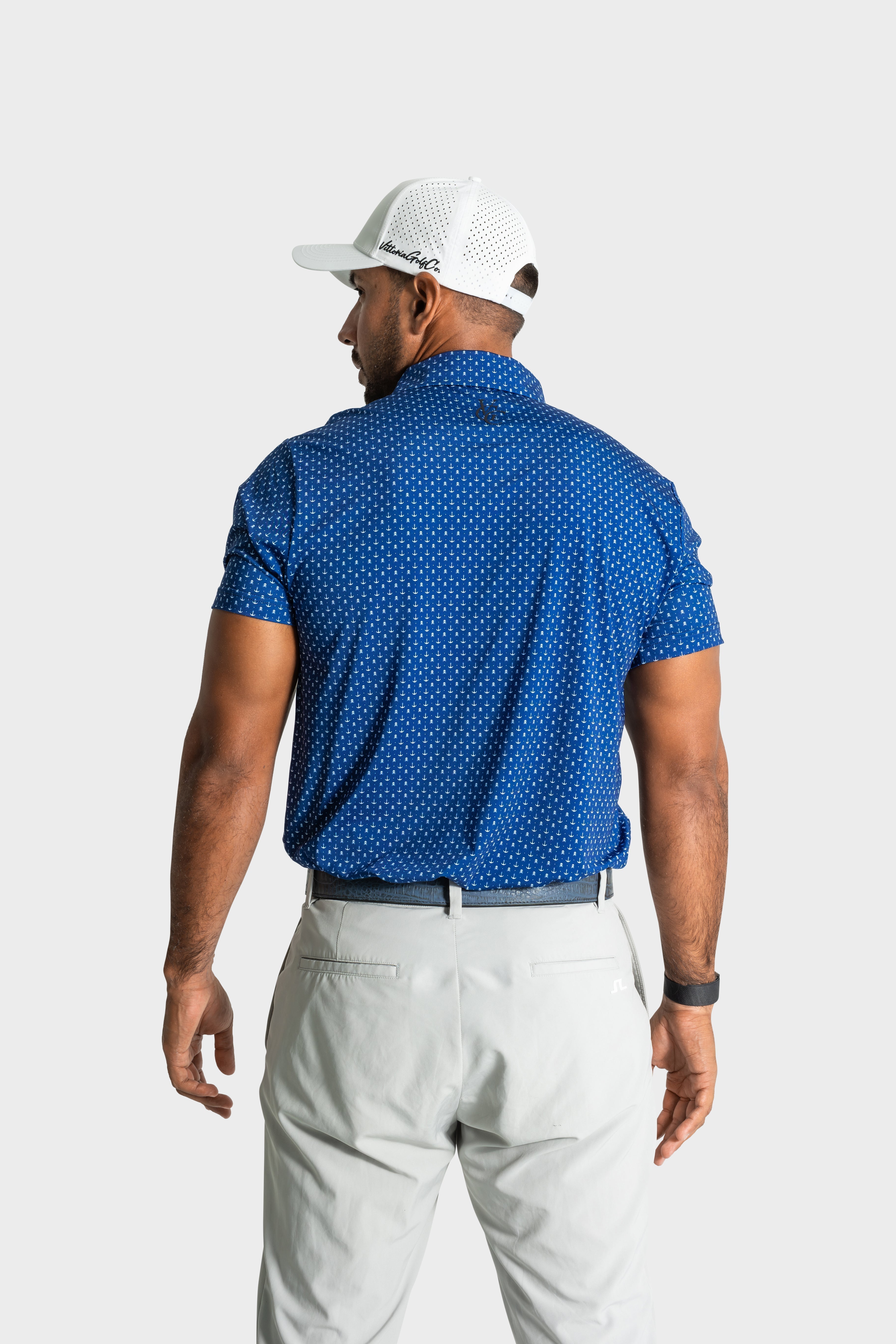 Back view of man wearing The Deadman polo in blue with white golf cap and light trousers