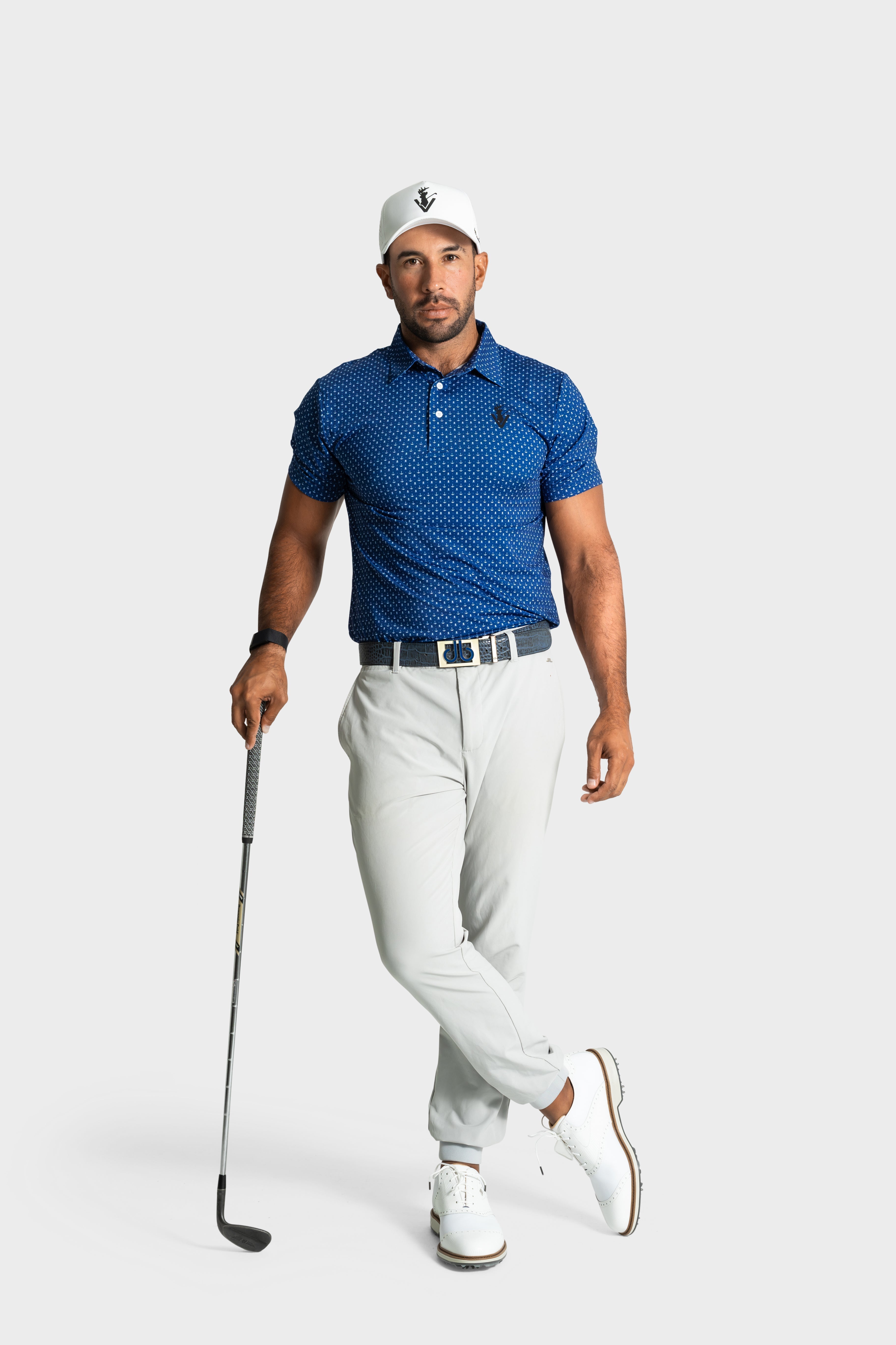 Man wearing The Deadman polo by VittoriaGolfco, white pants, and cap holding a golf club
