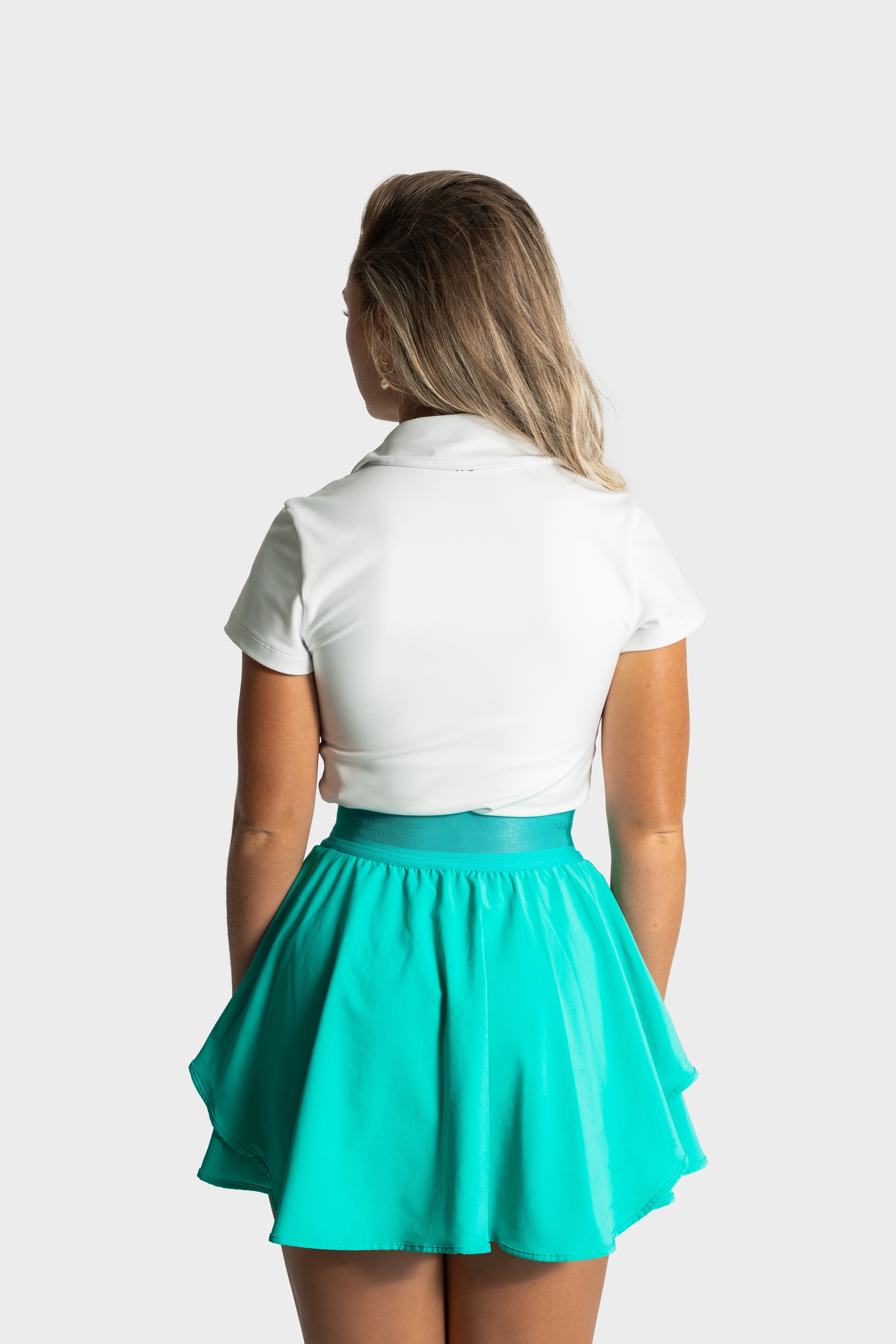 Woman wearing turquoise Blossom golf skirt and white polo shirt, back view, isolated on white background