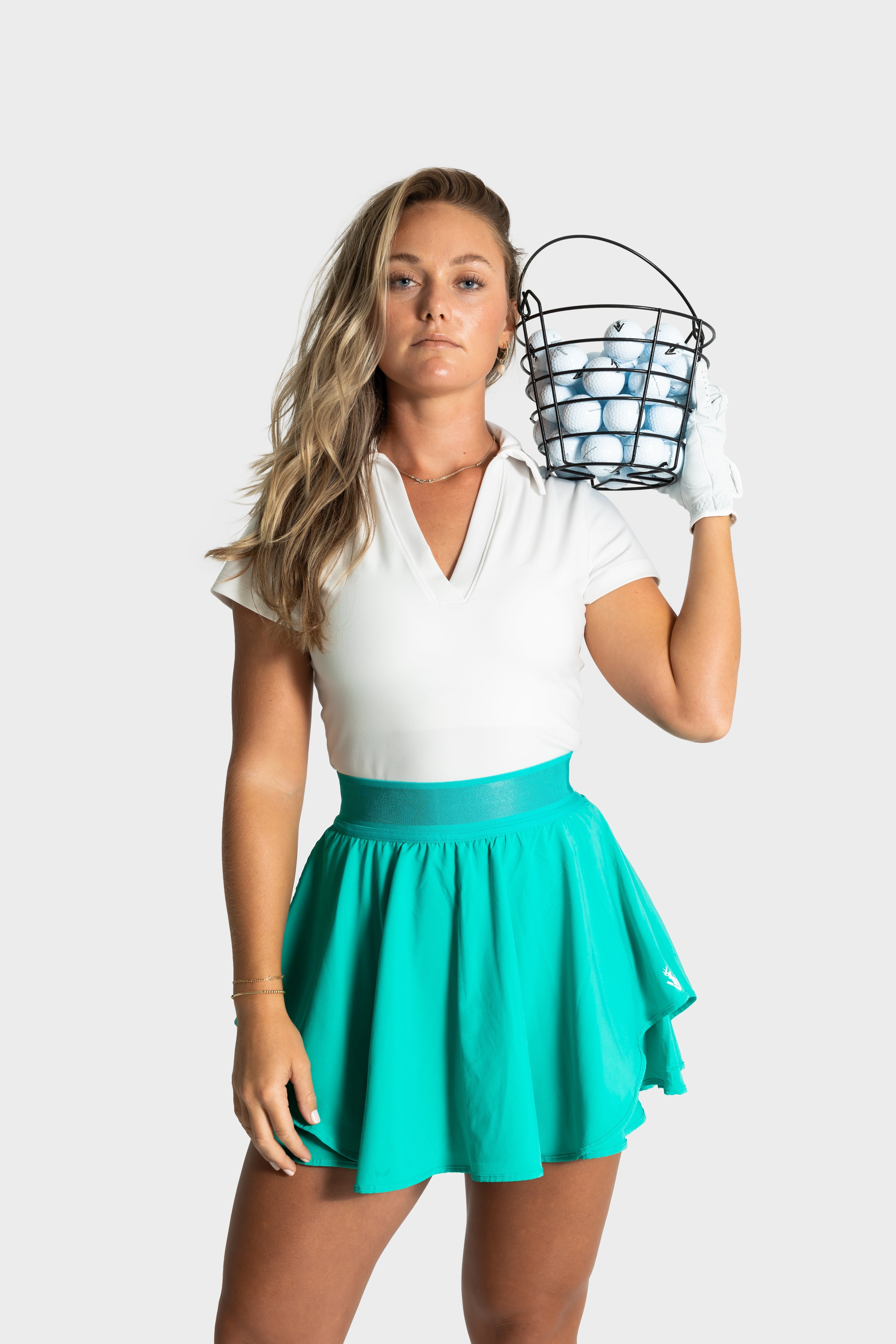 Woman wearing turquoise Blossom golf skirt holding basket of golf balls on shoulder