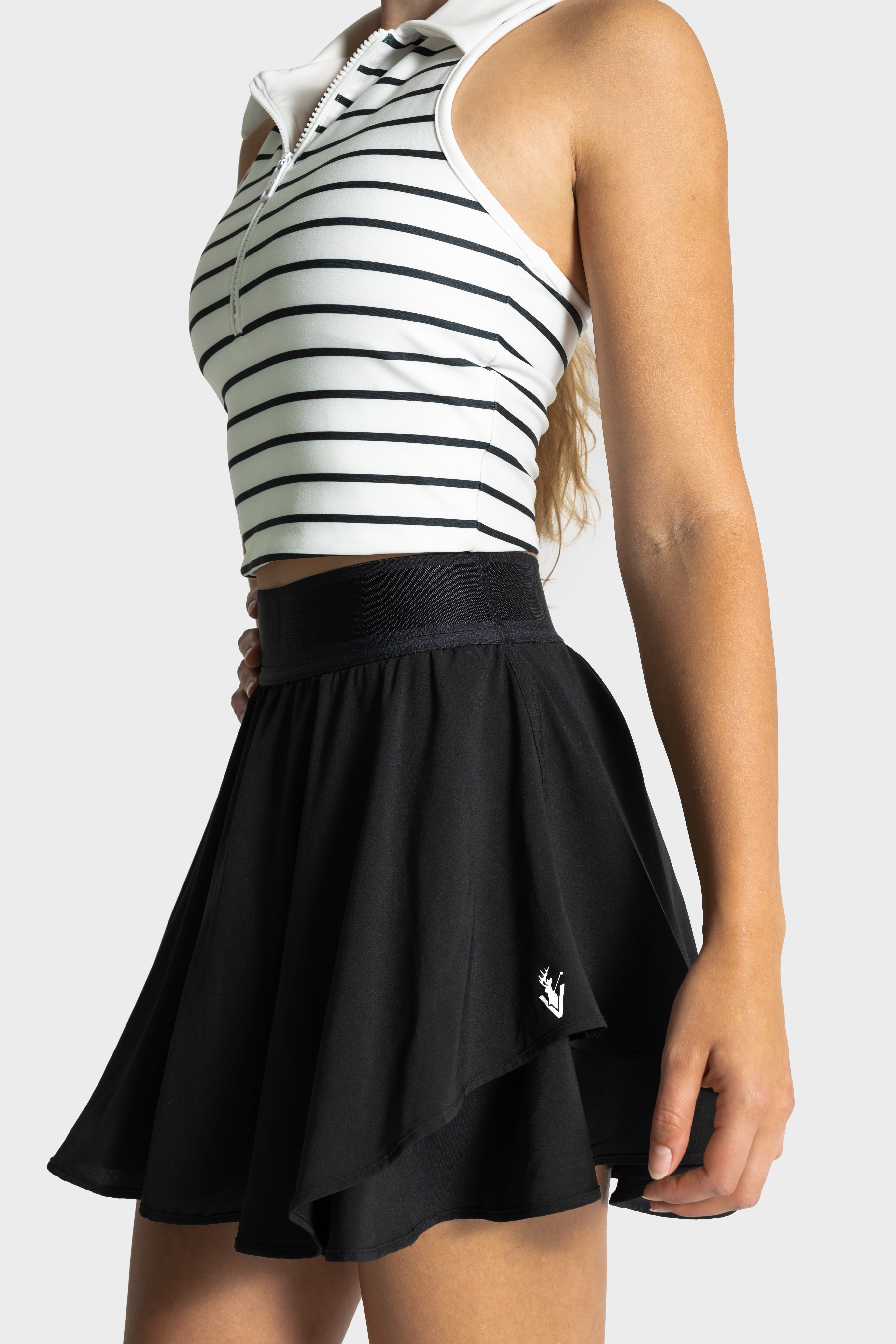 Woman wearing a black Blossom golf skirt with built-in compression shorts and a striped sleeveless golf top