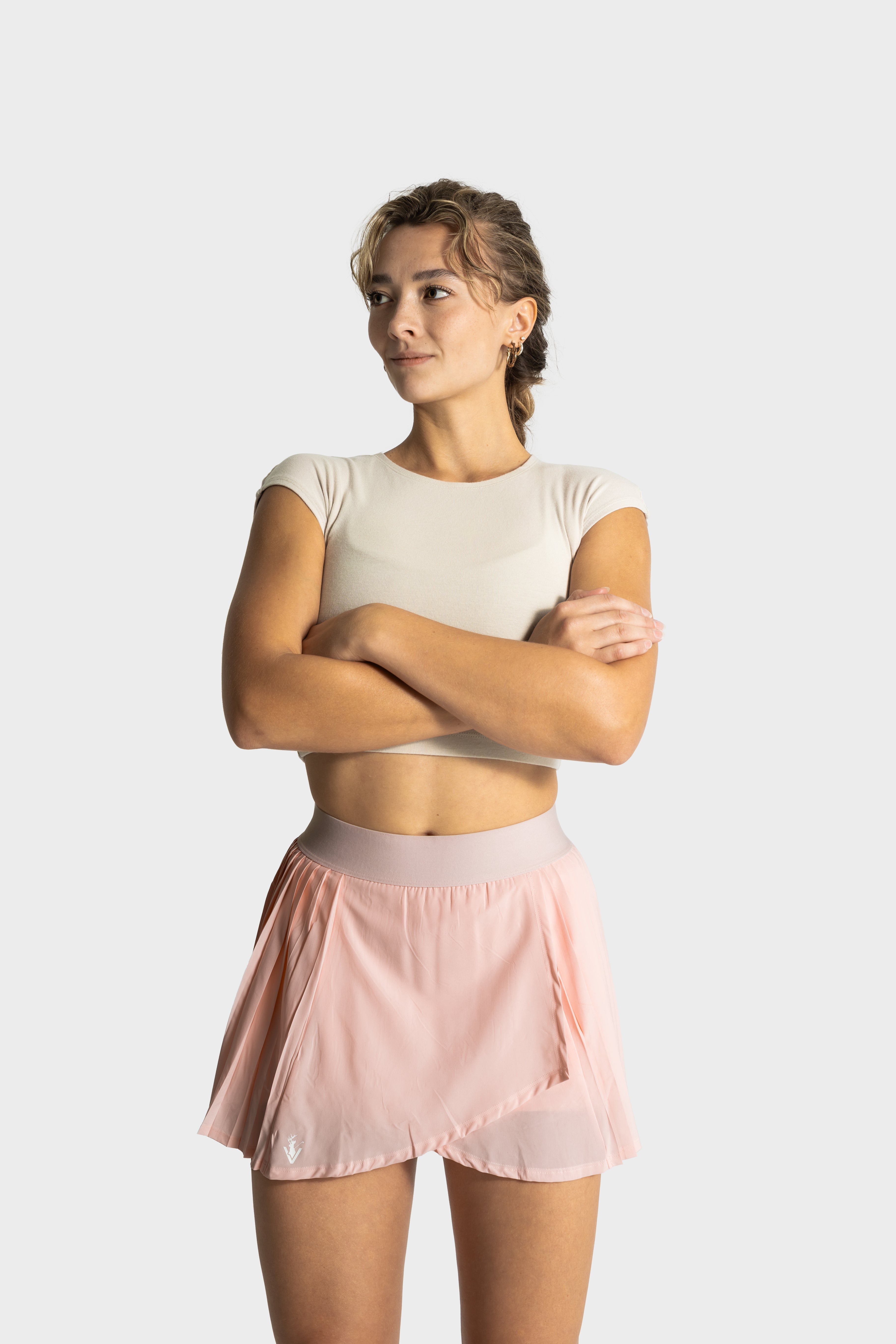 Woman wearing blush pink Perfetta golf skirt by Vittoria Golf Co. with fitted beige crop top against white background