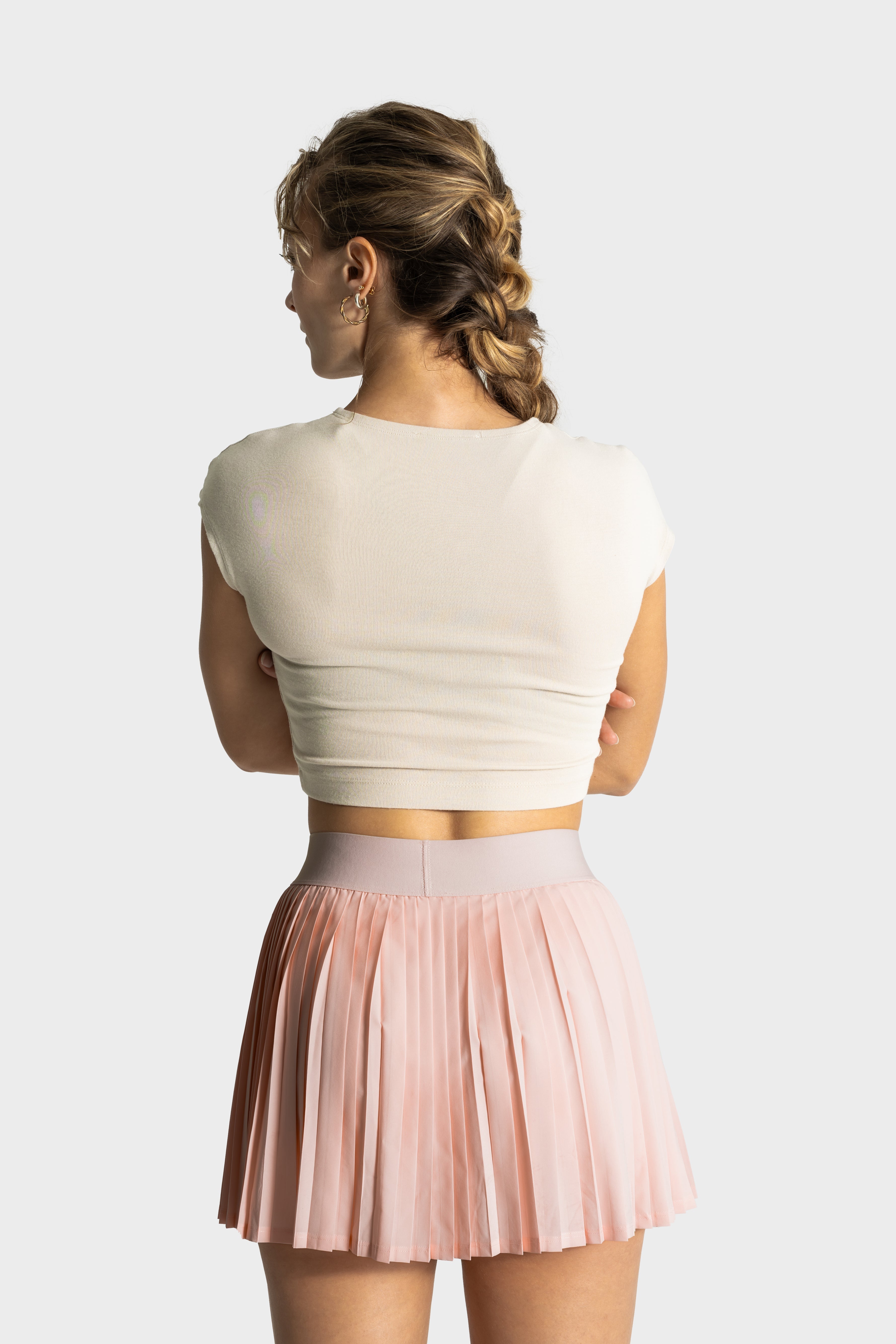 Woman wearing a light pink pleated Perfetta golf skirt by Vittoria Golf Co. and a white cropped top from the back view