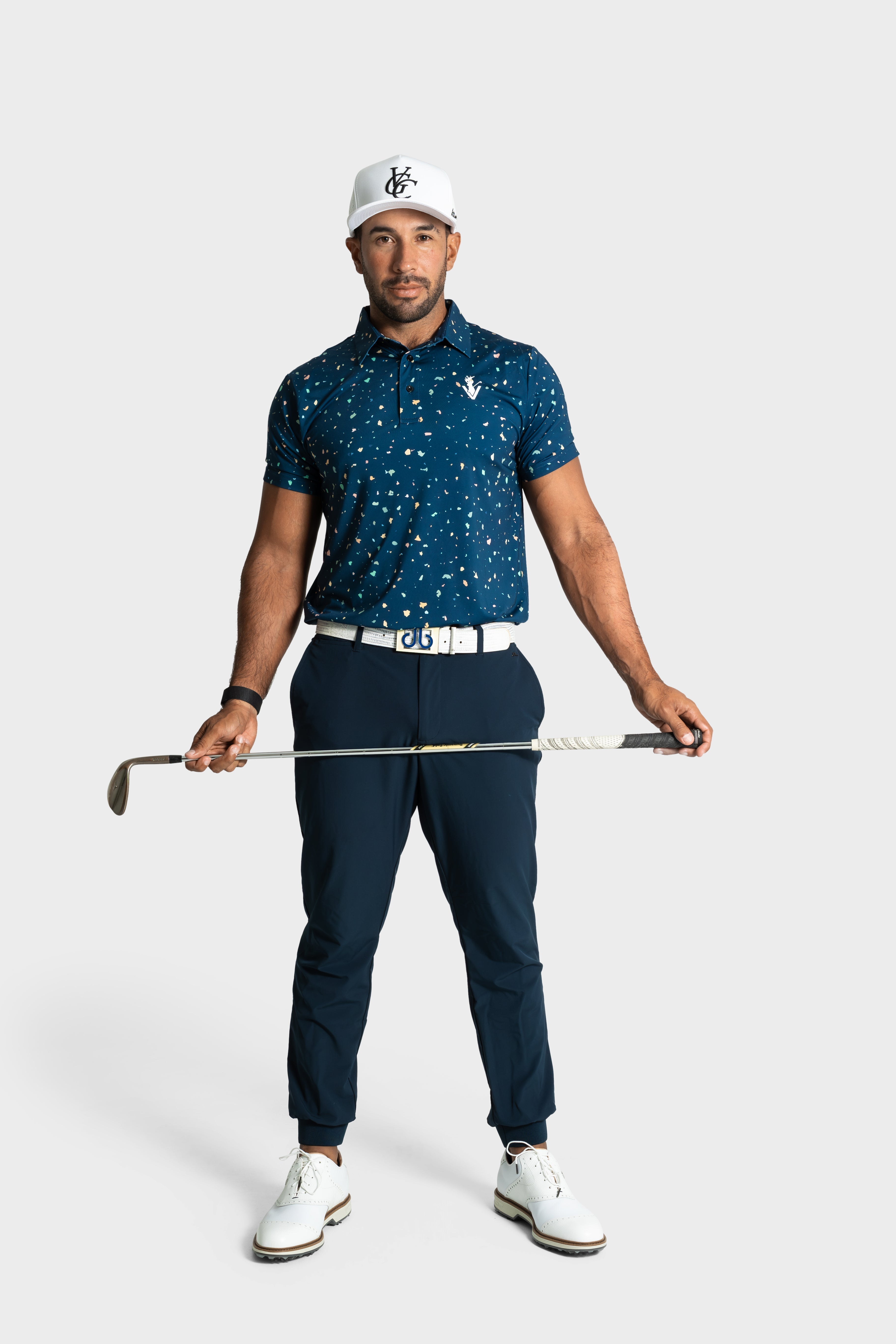 Man wearing The Underlay polo holding a golf club standing against a white background
