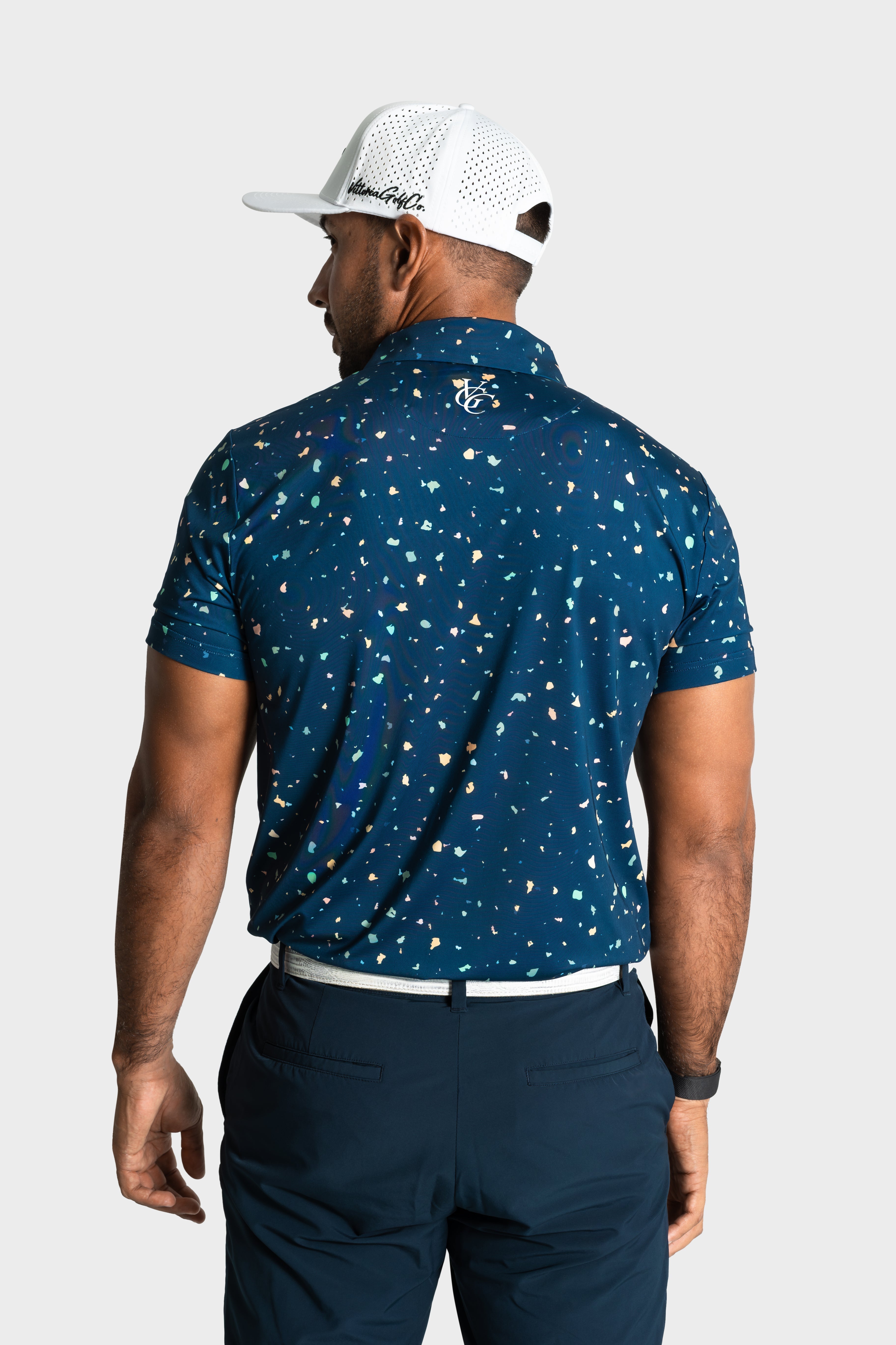 Back view of man wearing The Underlay polo with multicolor print and white cap on golf course
