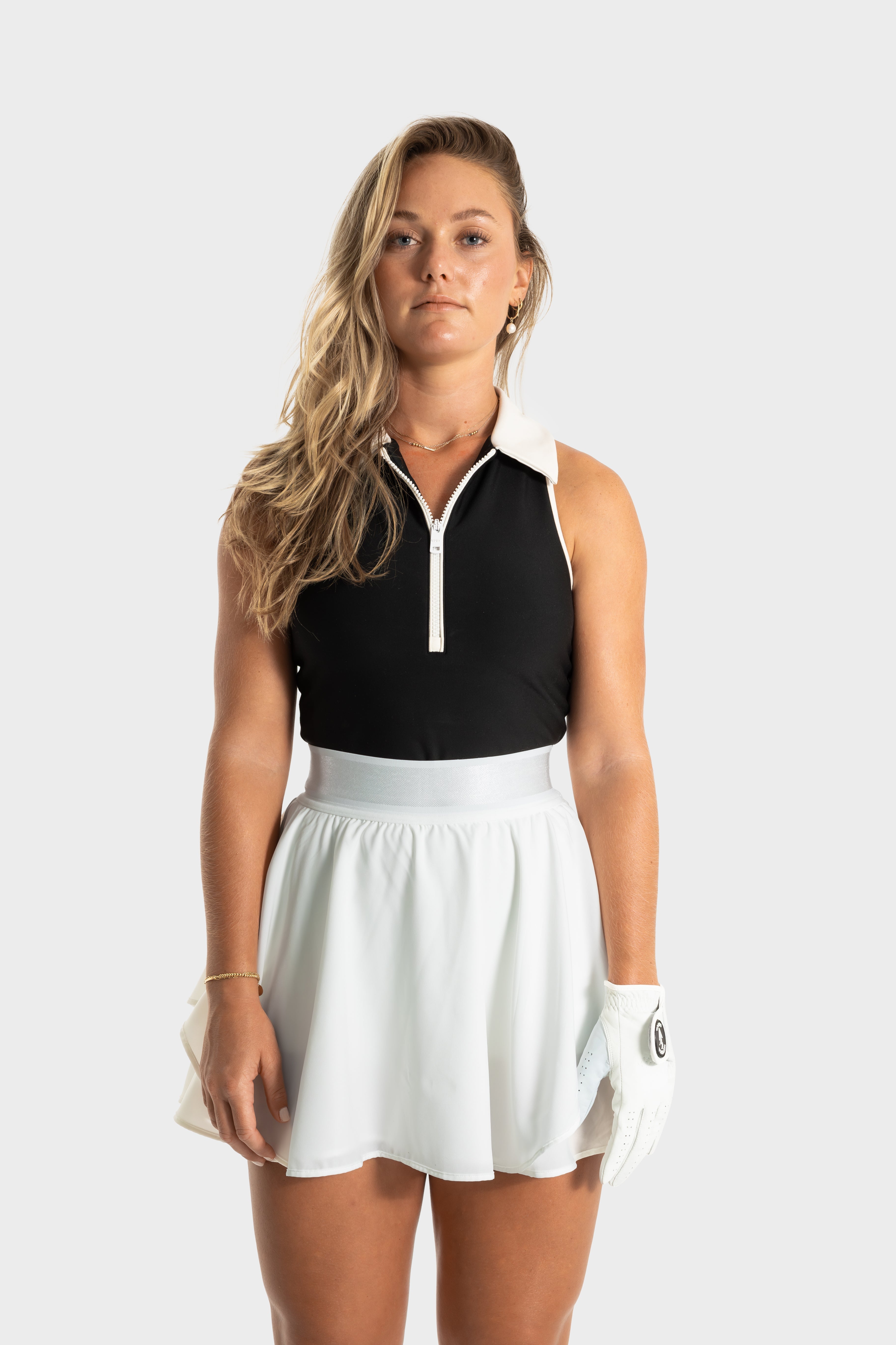woman wearing white Blossom golf skirt and black sleeveless golf top standing against plain background