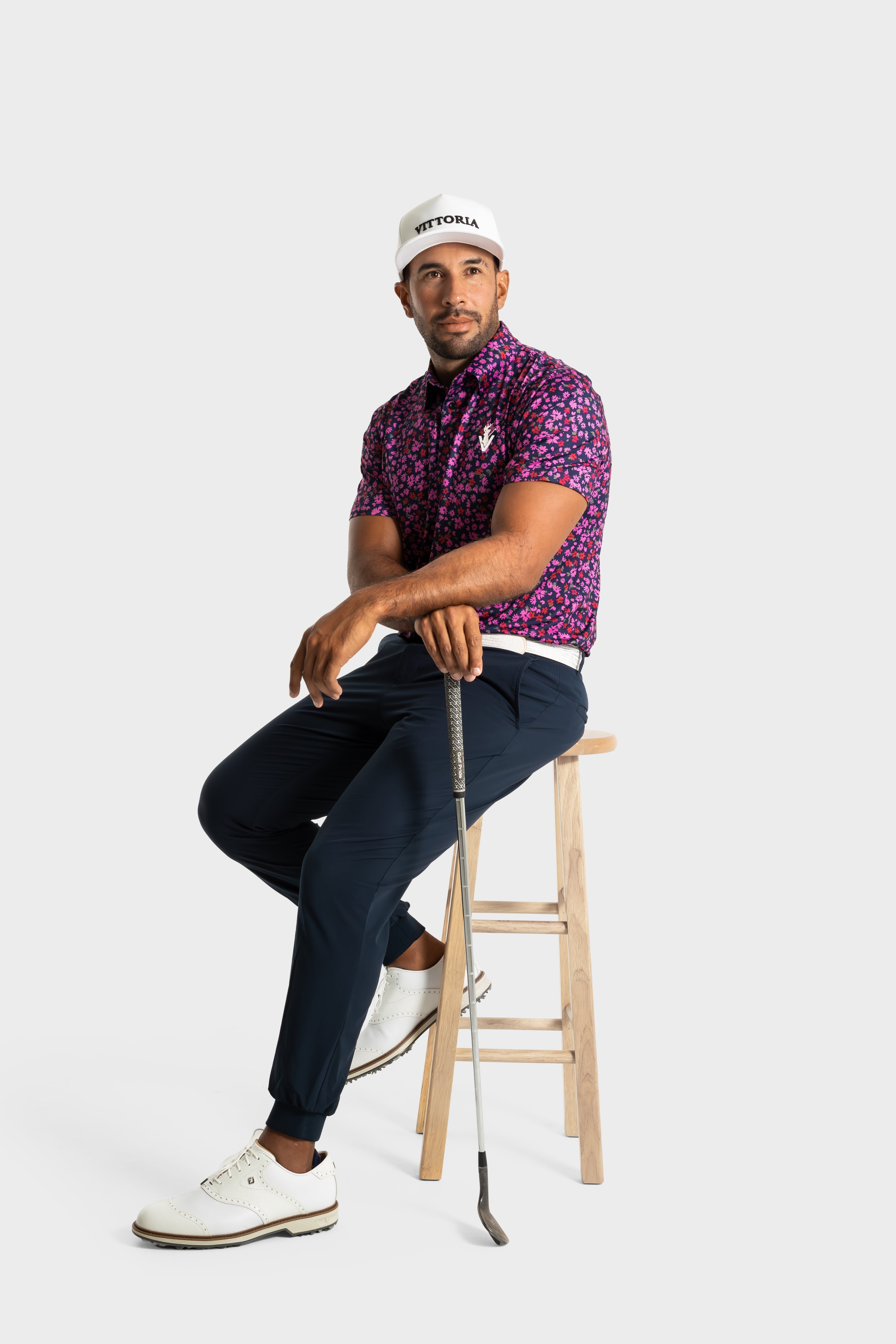 Man wearing The Secret Garden polo shirt by VittoriaGolfco sitting on stool with golf club