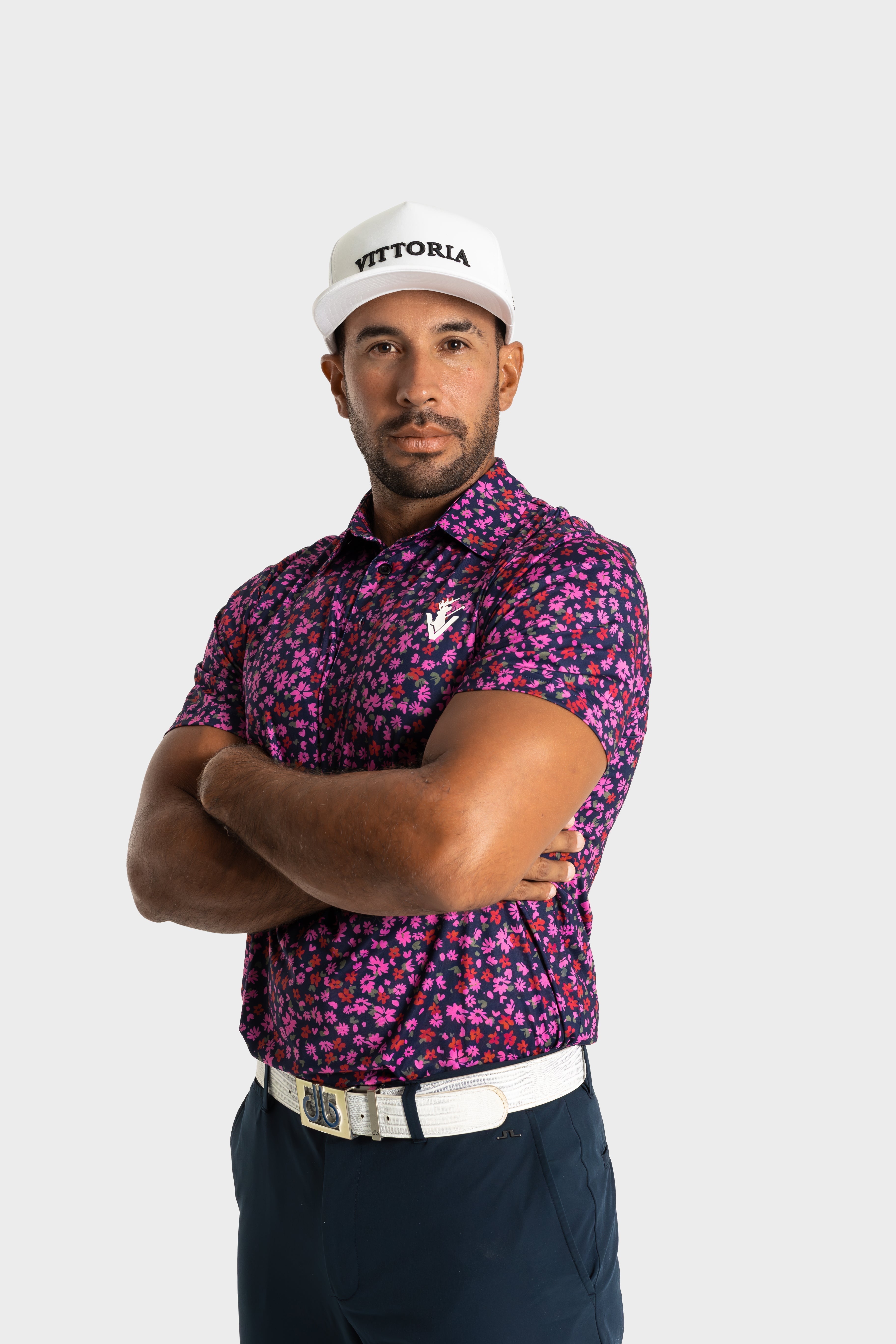 Man wearing The Secret Garden floral golf polo by VittoriaGolfco with white cap and belt