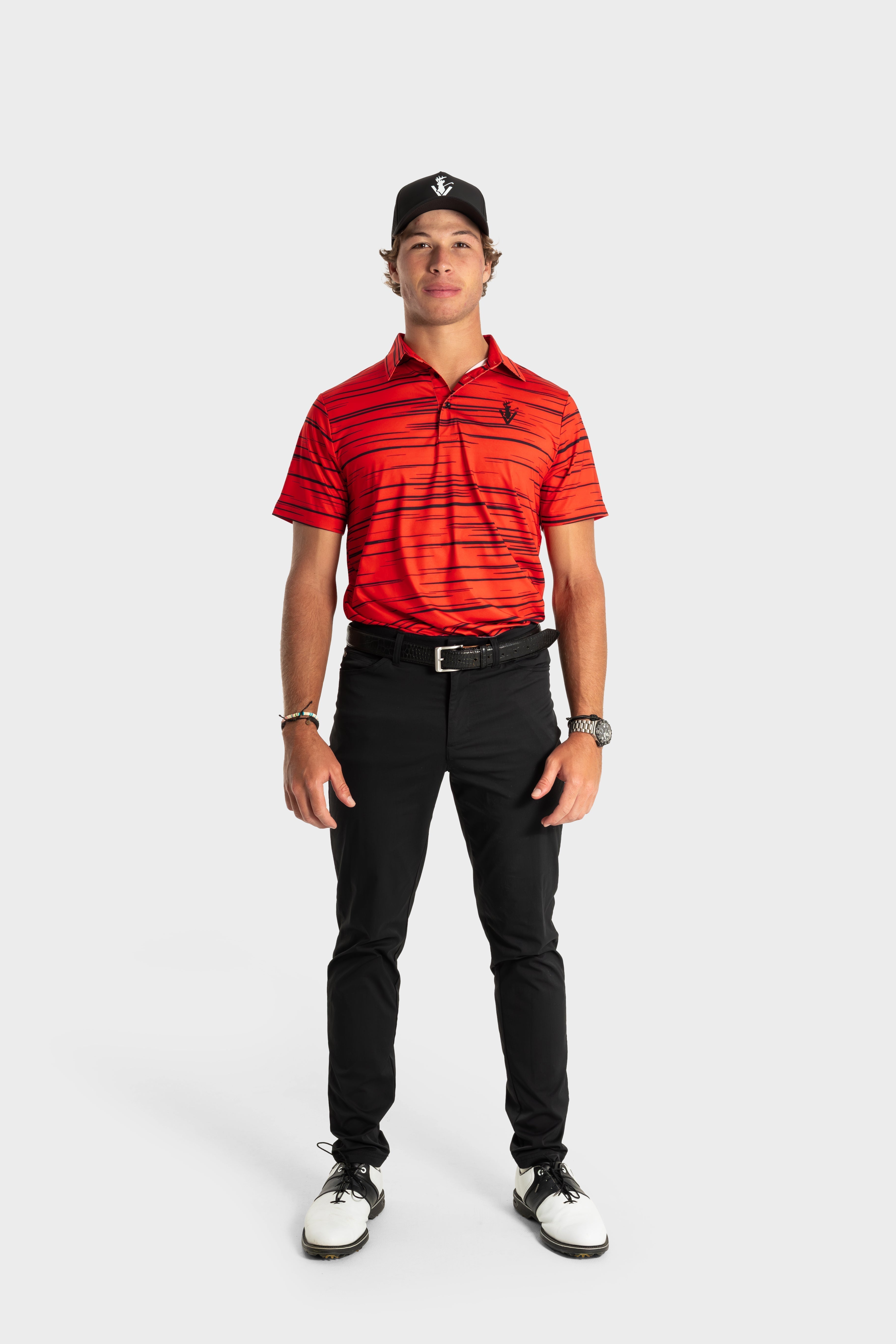 Man wearing red striped The Sunday Polo shirt with black pants and cap standing against white background