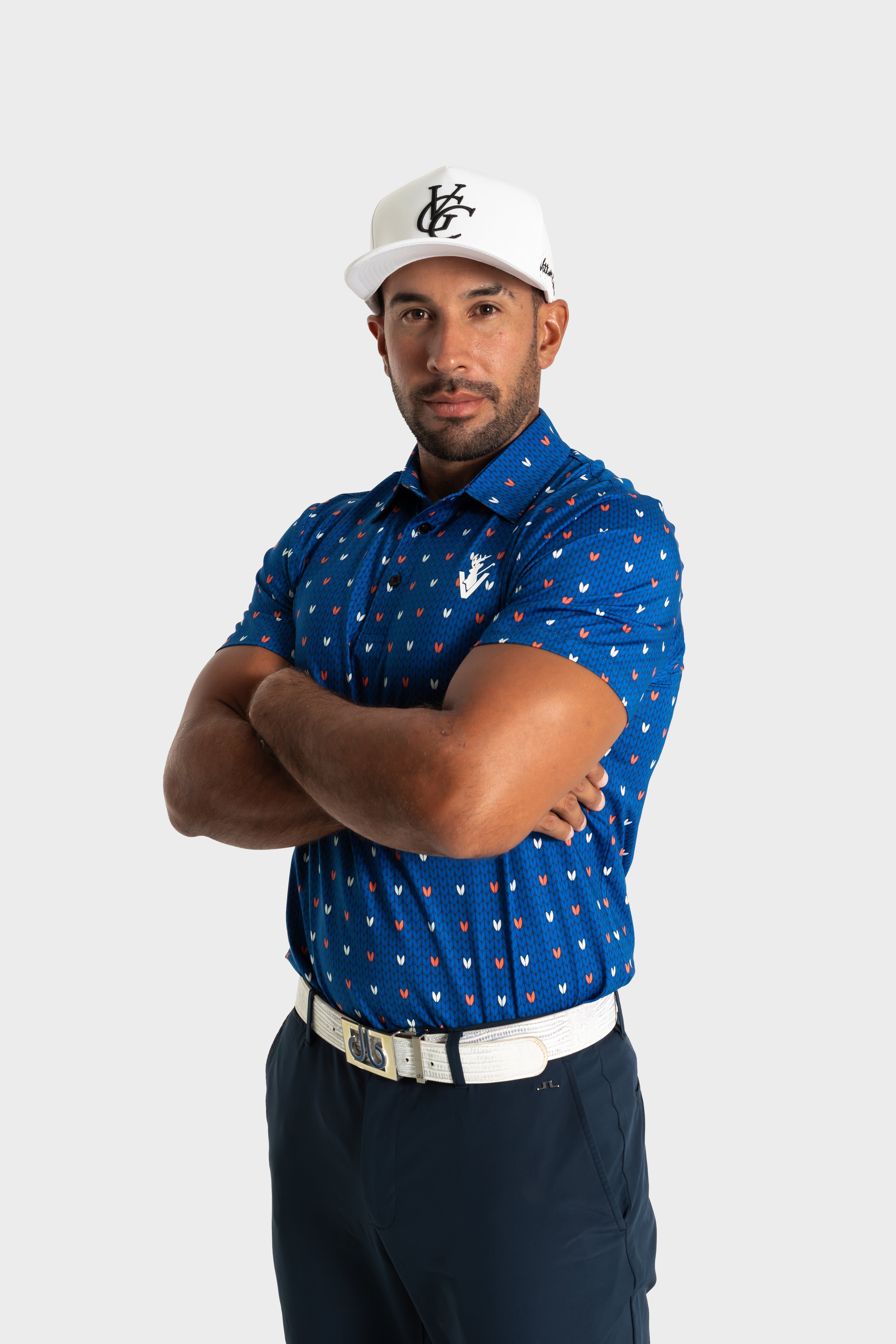 Male model wearing blue patterned The Knitted polo by VittoriaGolfco, paired with white cap and belt, standing with arms crossed