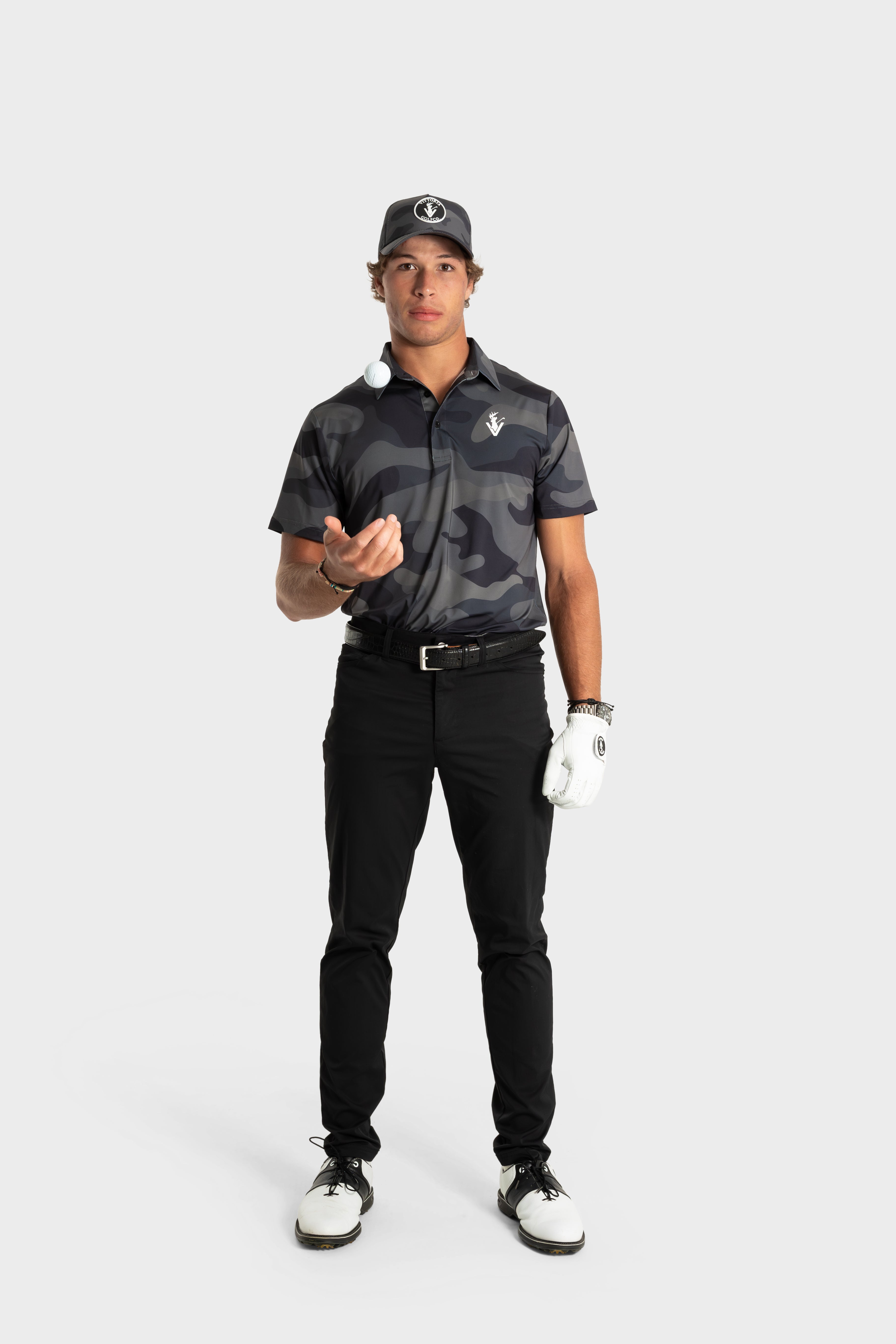 Male golfer wearing The Invincible polo by VittoriaGolfco in black camo standing with golf ball on finger