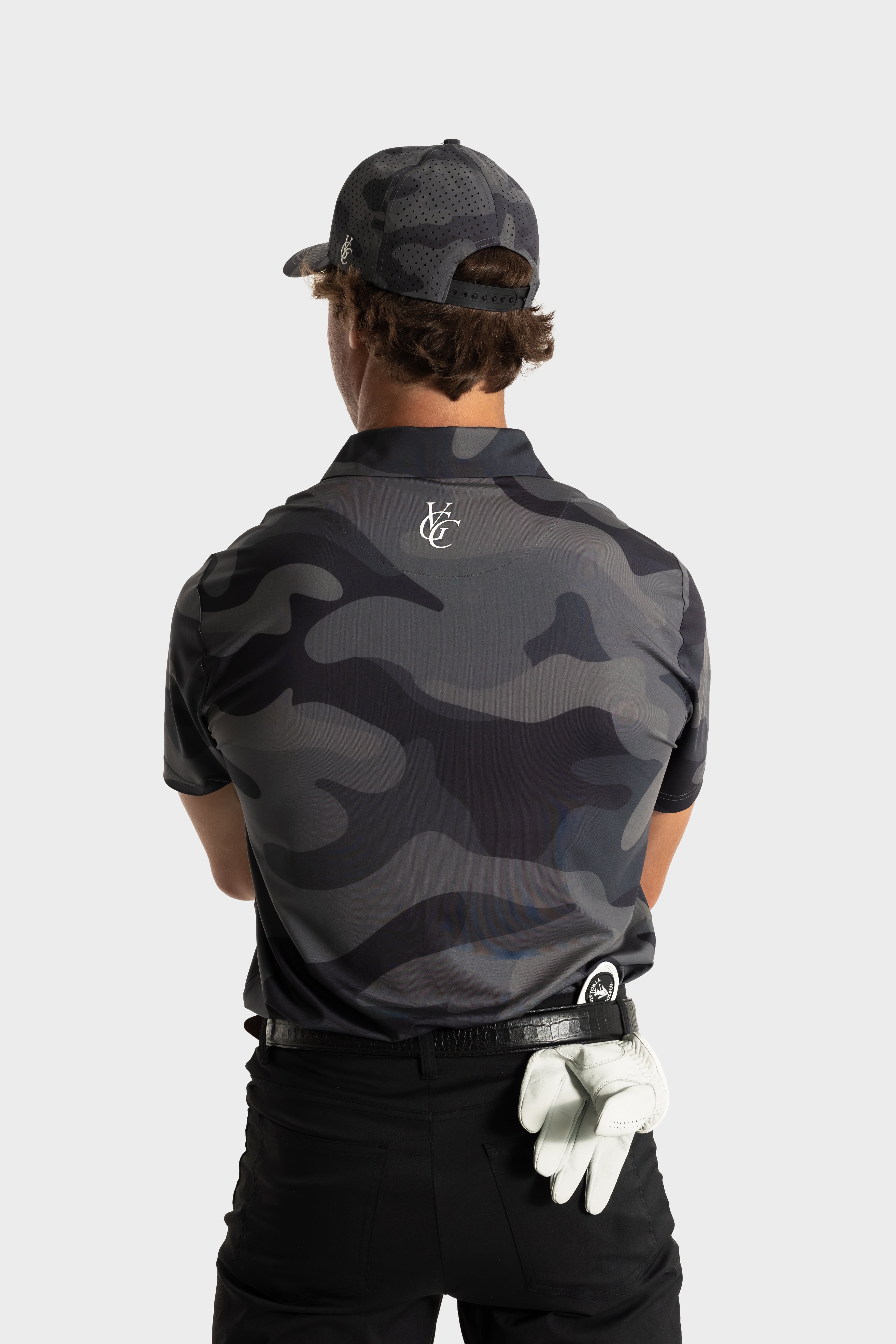 Back view of man wearing The Invincible polo with dark camouflage pattern and matching cap