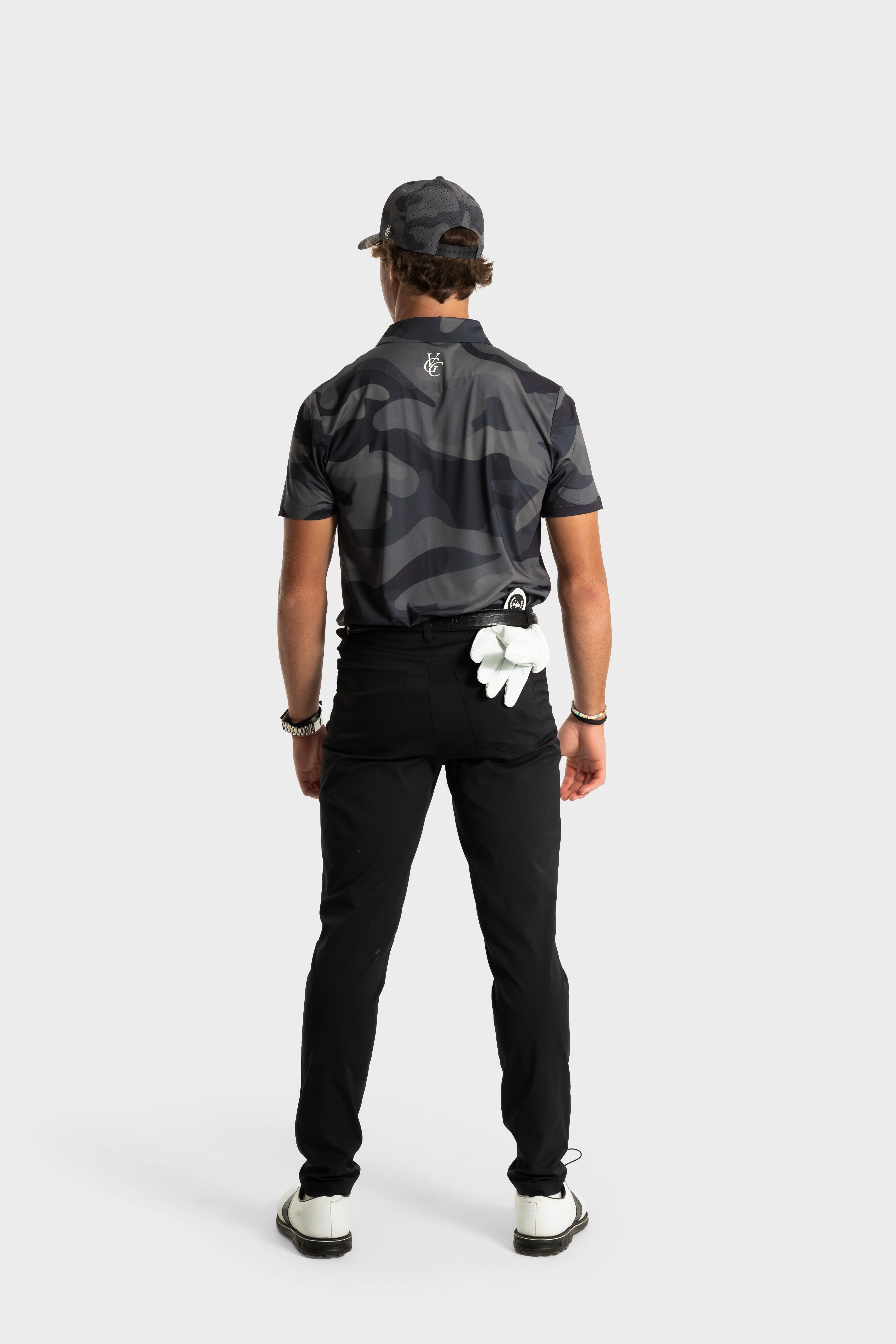 Man wearing black and gray camo print The Invincible polo standing with golf glove tucked in back pocket