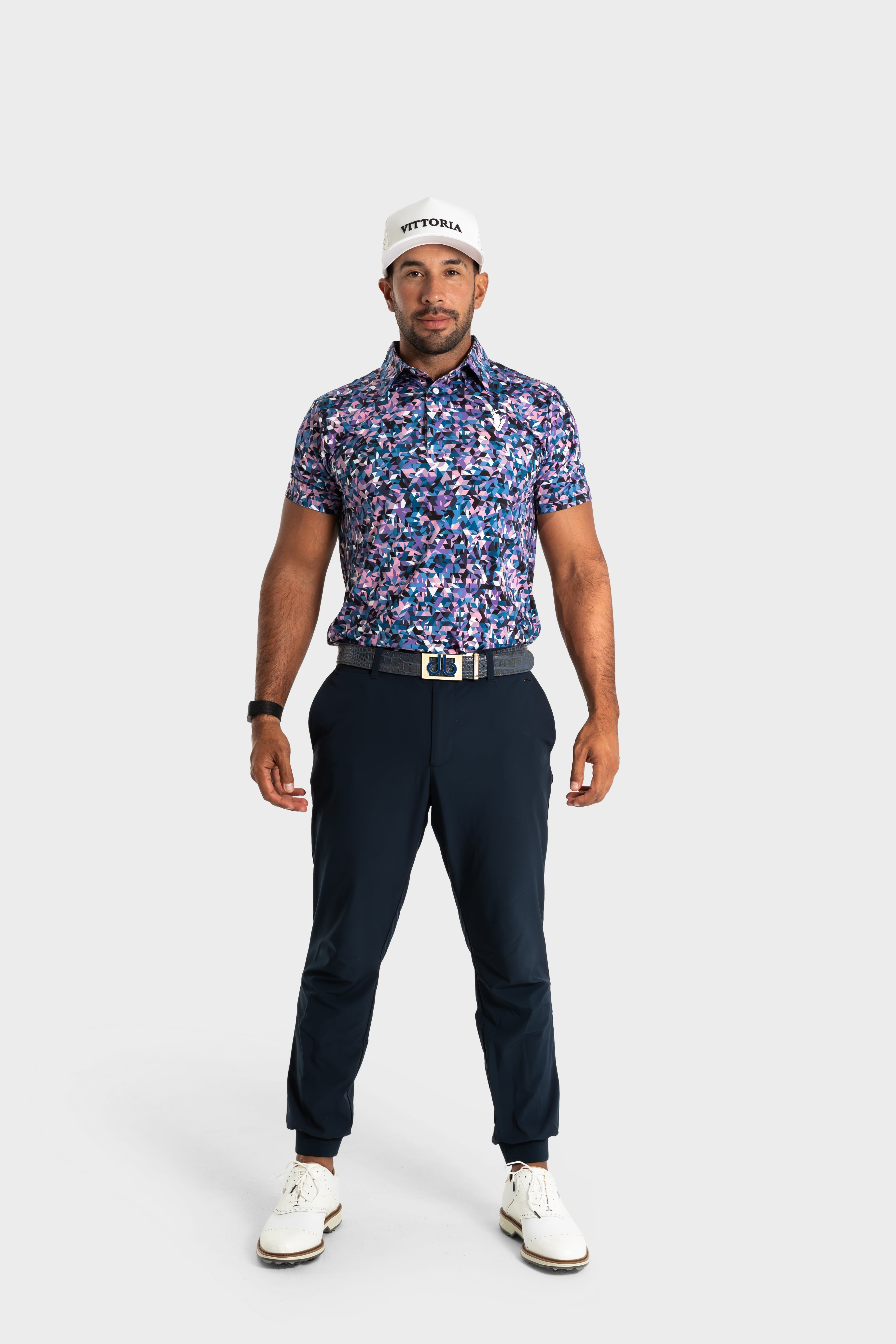 Man wearing The Geo polo with bold geometric patterns and black pants standing against white background