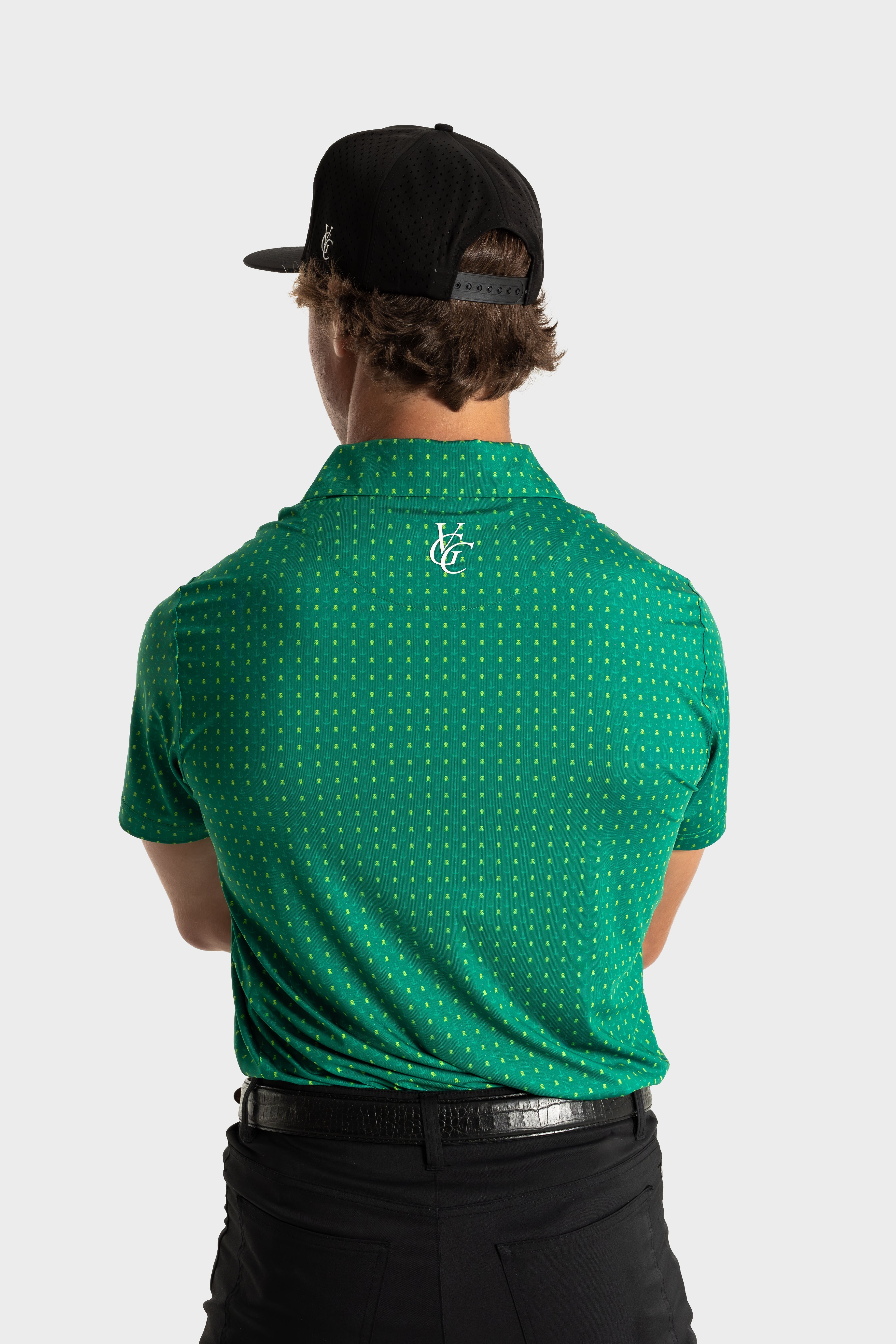 Back view of man wearing green Skullzalea Golf Polo with tiny skull pattern and black cap