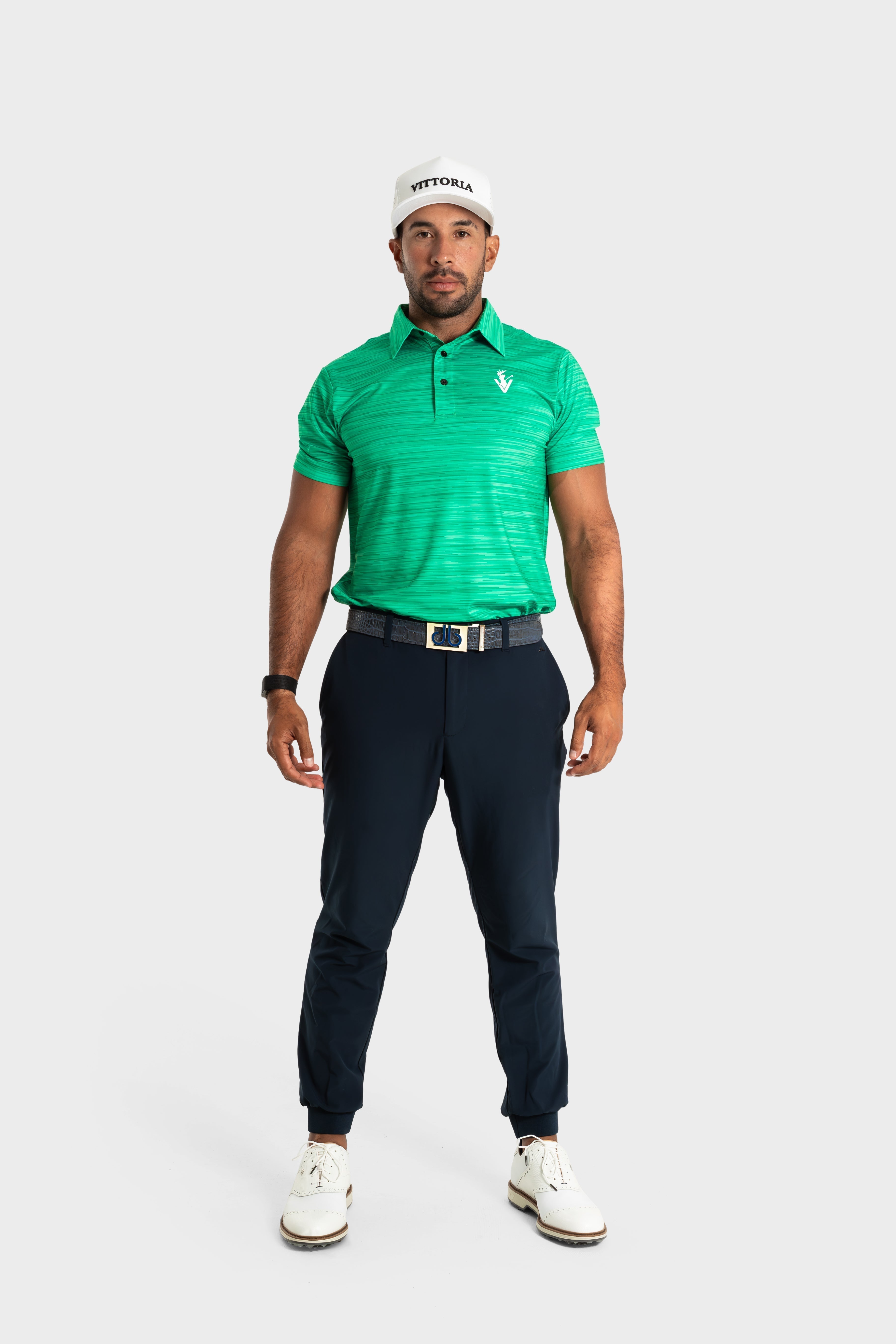 Male model wearing green The Pasture polo with navy pants and white golf shoes and cap on white background