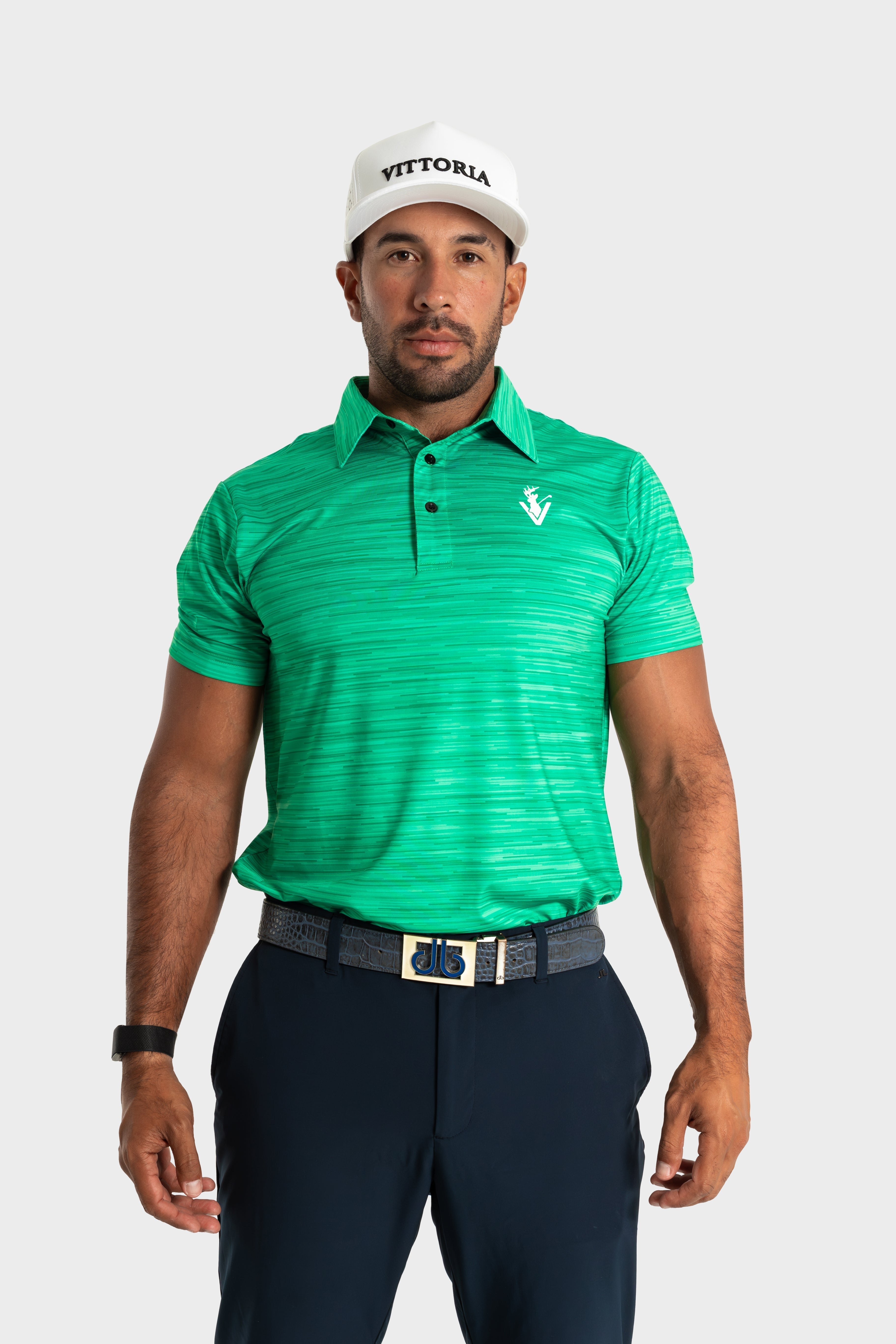 Man wearing green The Pasture polo by VittoriaGolfco with a white cap and navy pants