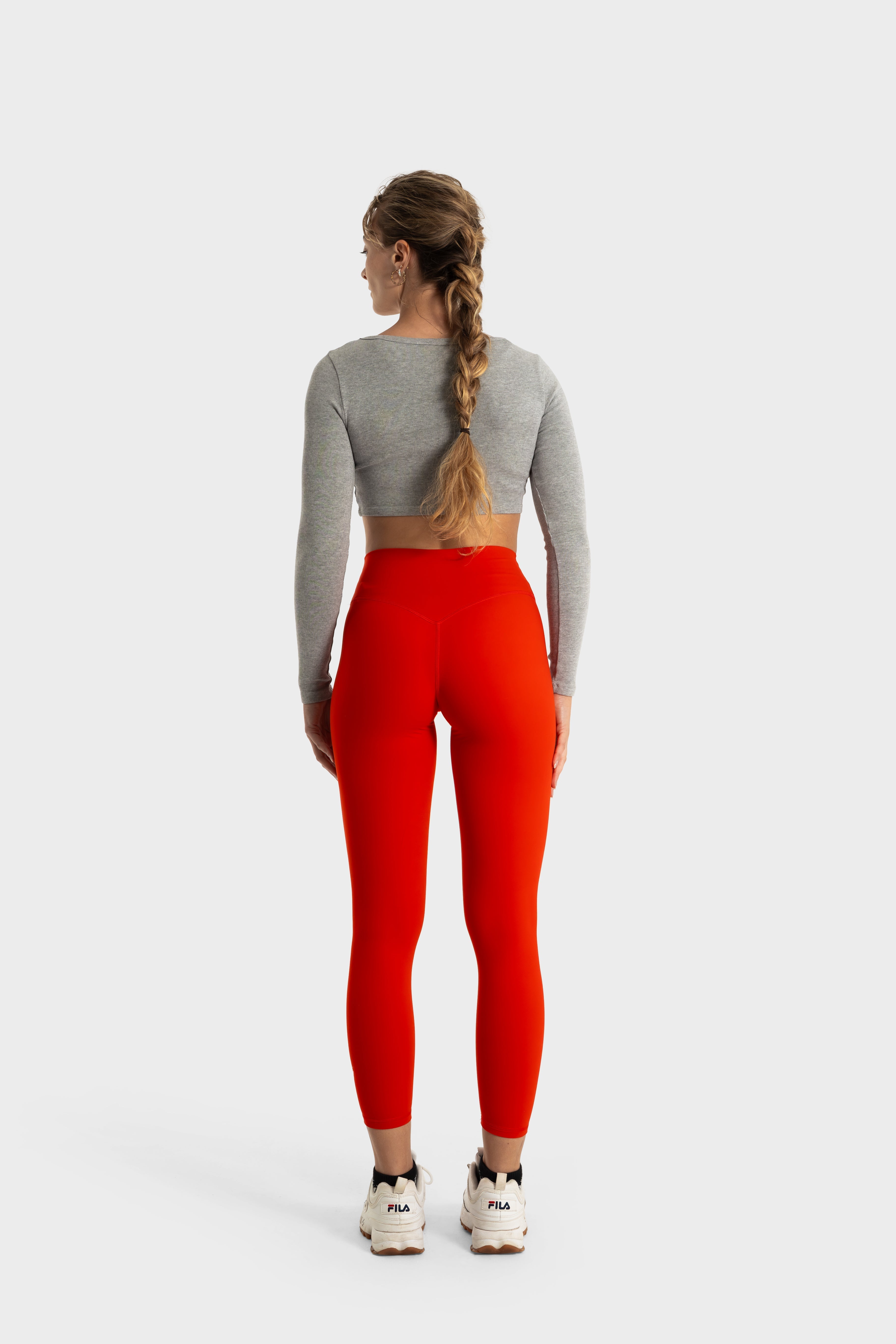 Woman wearing bright red Sollevare leggings and gray long-sleeve crop top standing with back view