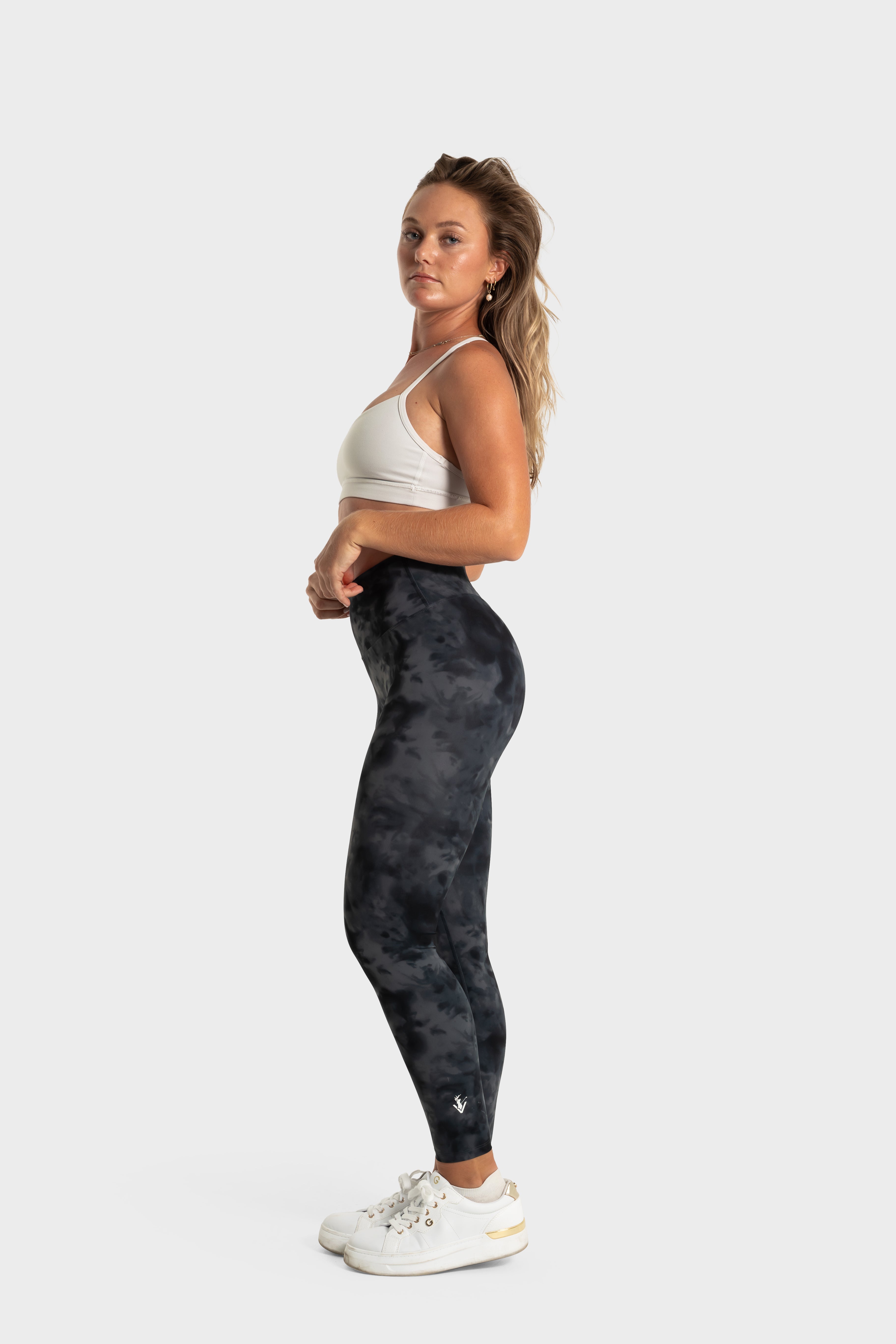 Woman wearing The Quelles black patterned leggings by VittoriaGolfCo with a white sports bra and white sneakers against a plain background