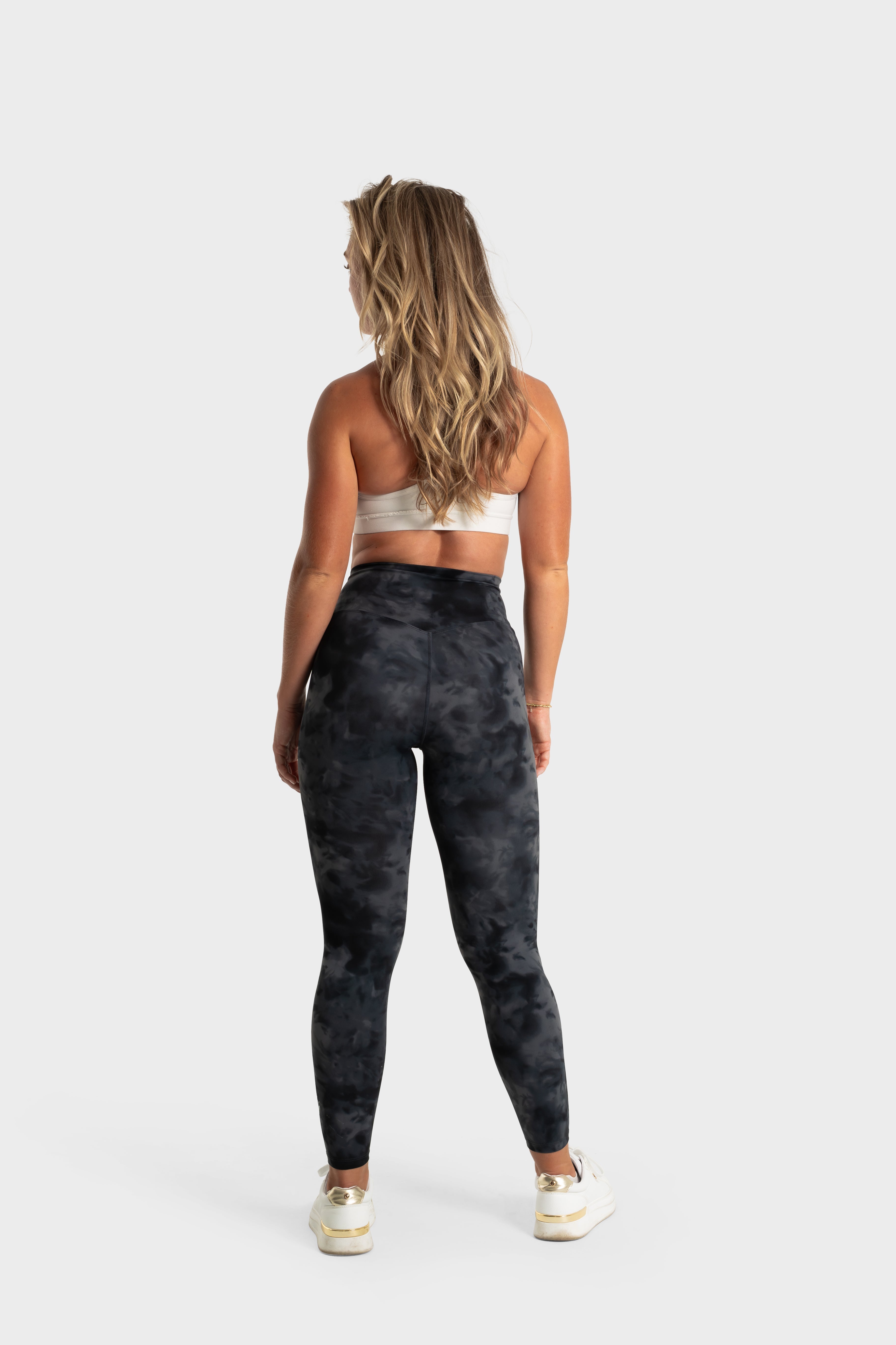 The Quelles leggings by VittoriaGolfCo in black camo, shown from the back on a woman in an active lifestyle pose