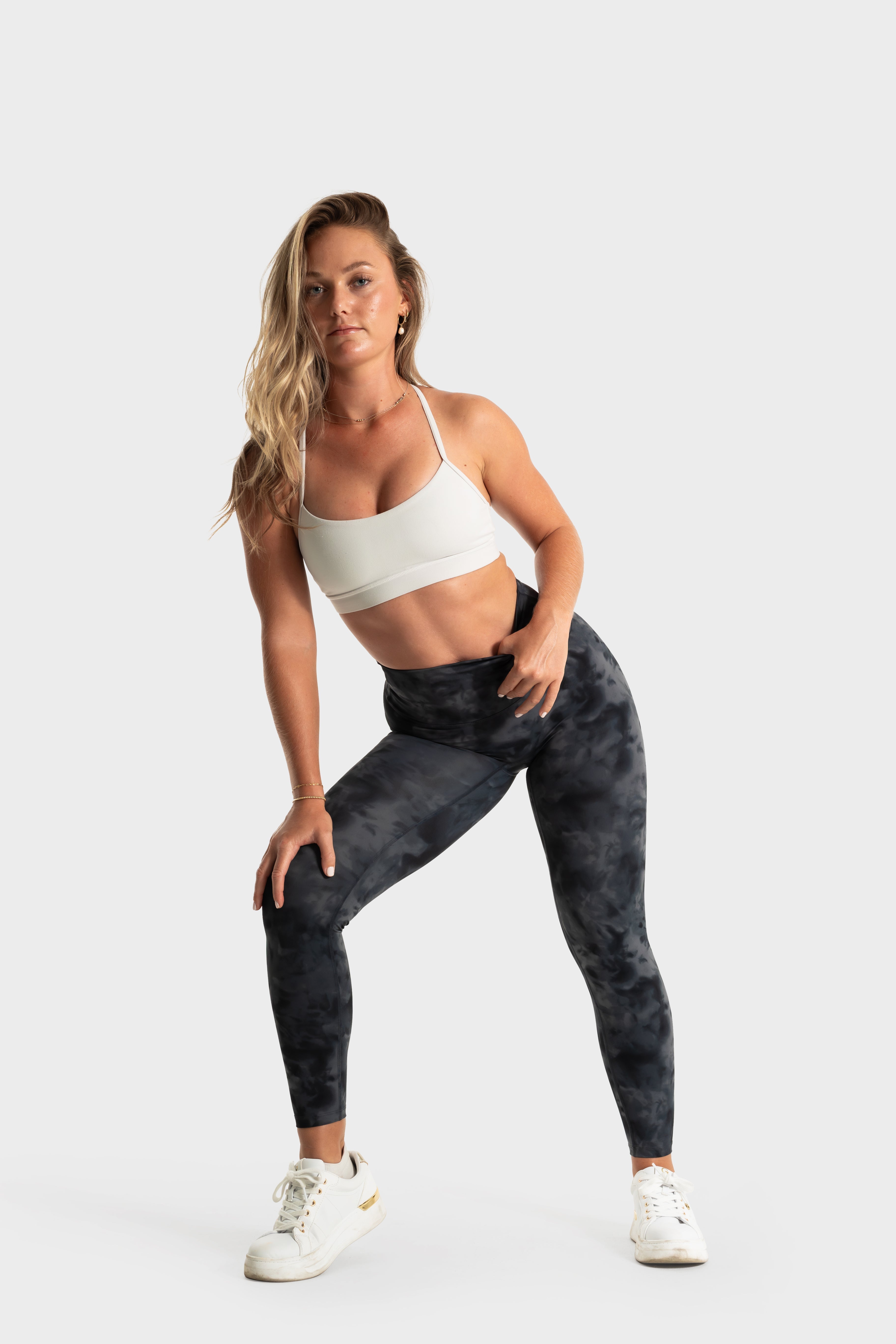 Woman wearing The Quelles black patterned leggings and white sports bra in active pose