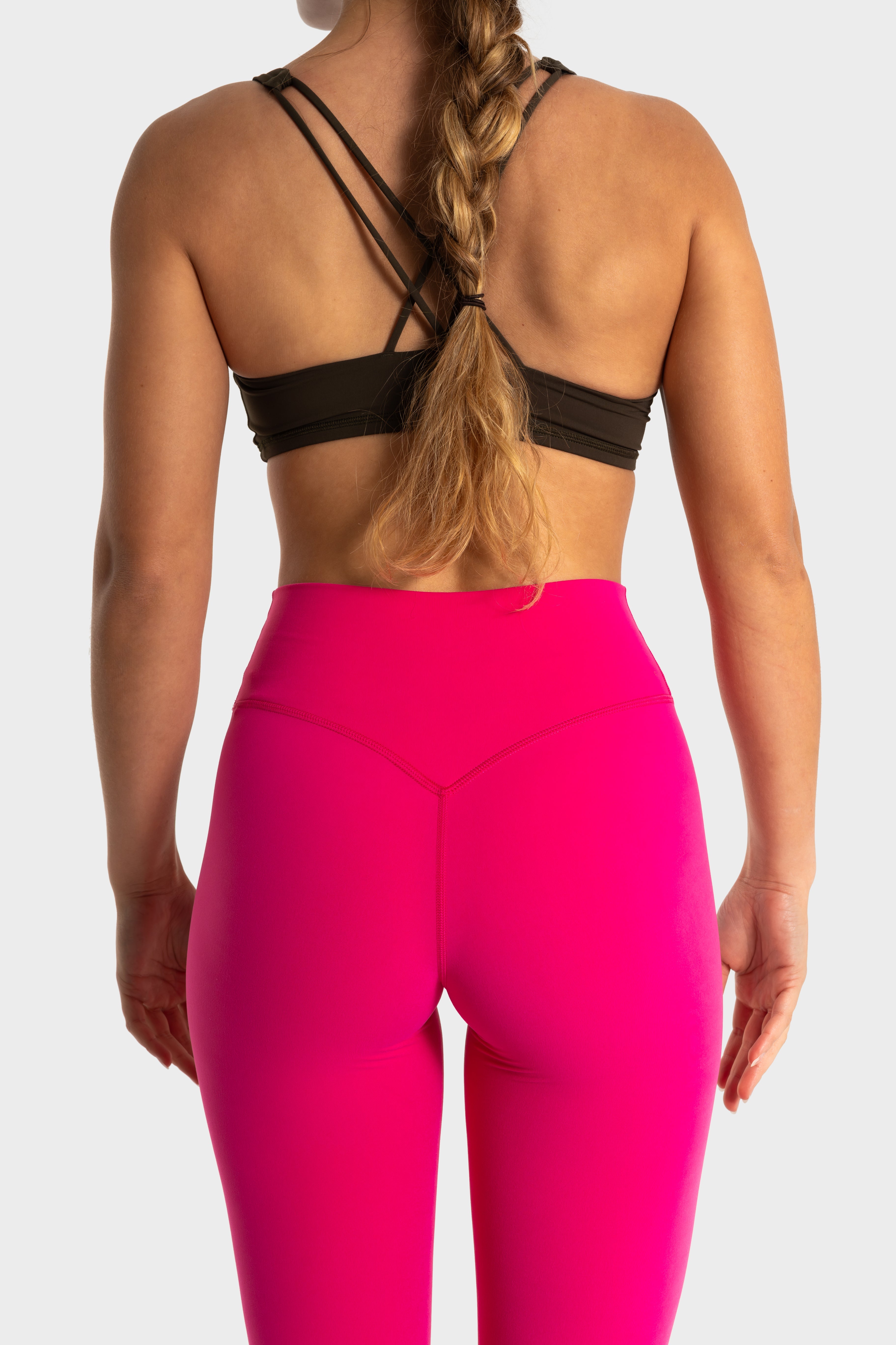 Woman wearing bright pink Sollevare leggings and black strappy sports bra from the back