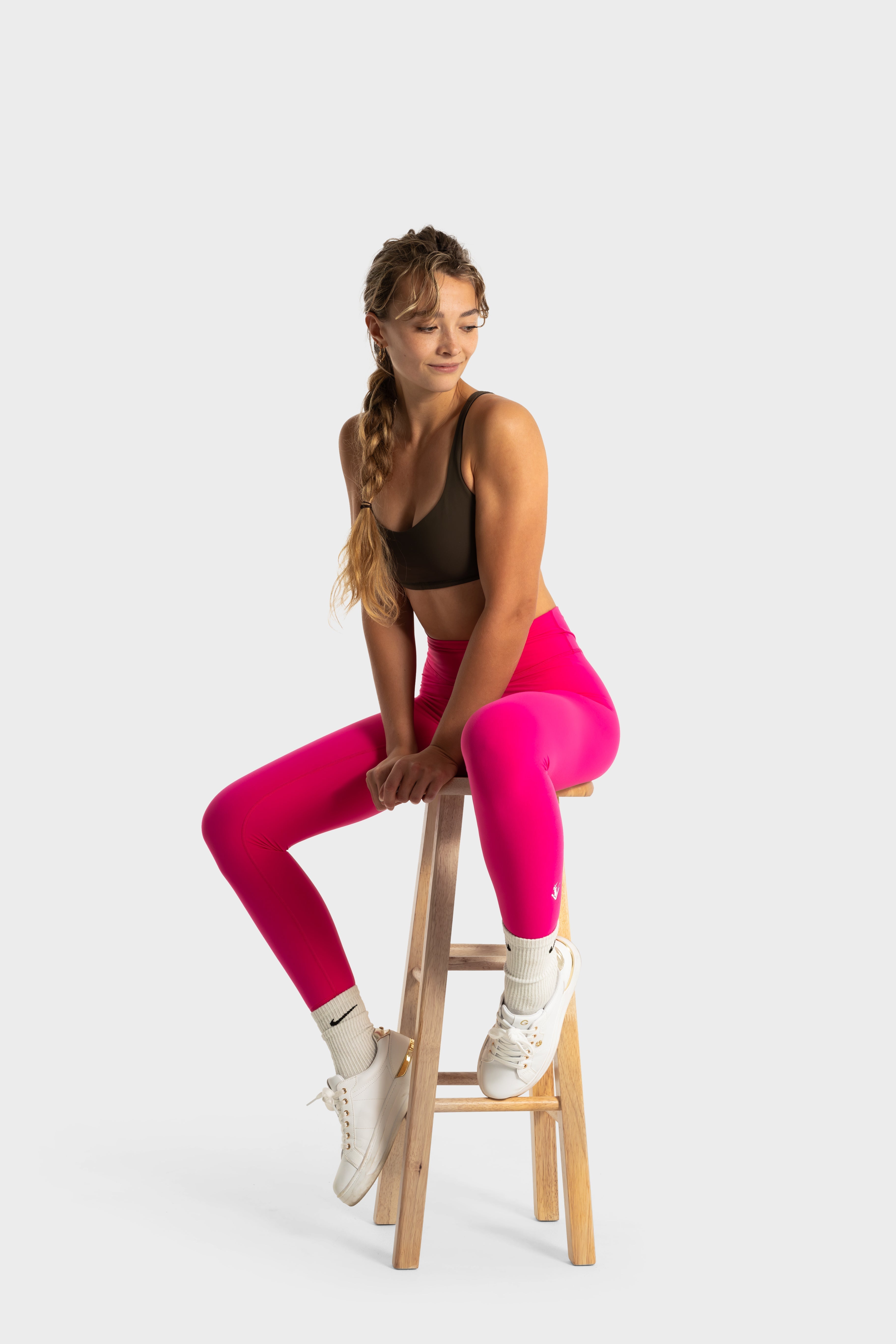 Woman wearing bright pink Sollevare leggings sitting on a wooden stool against a white background