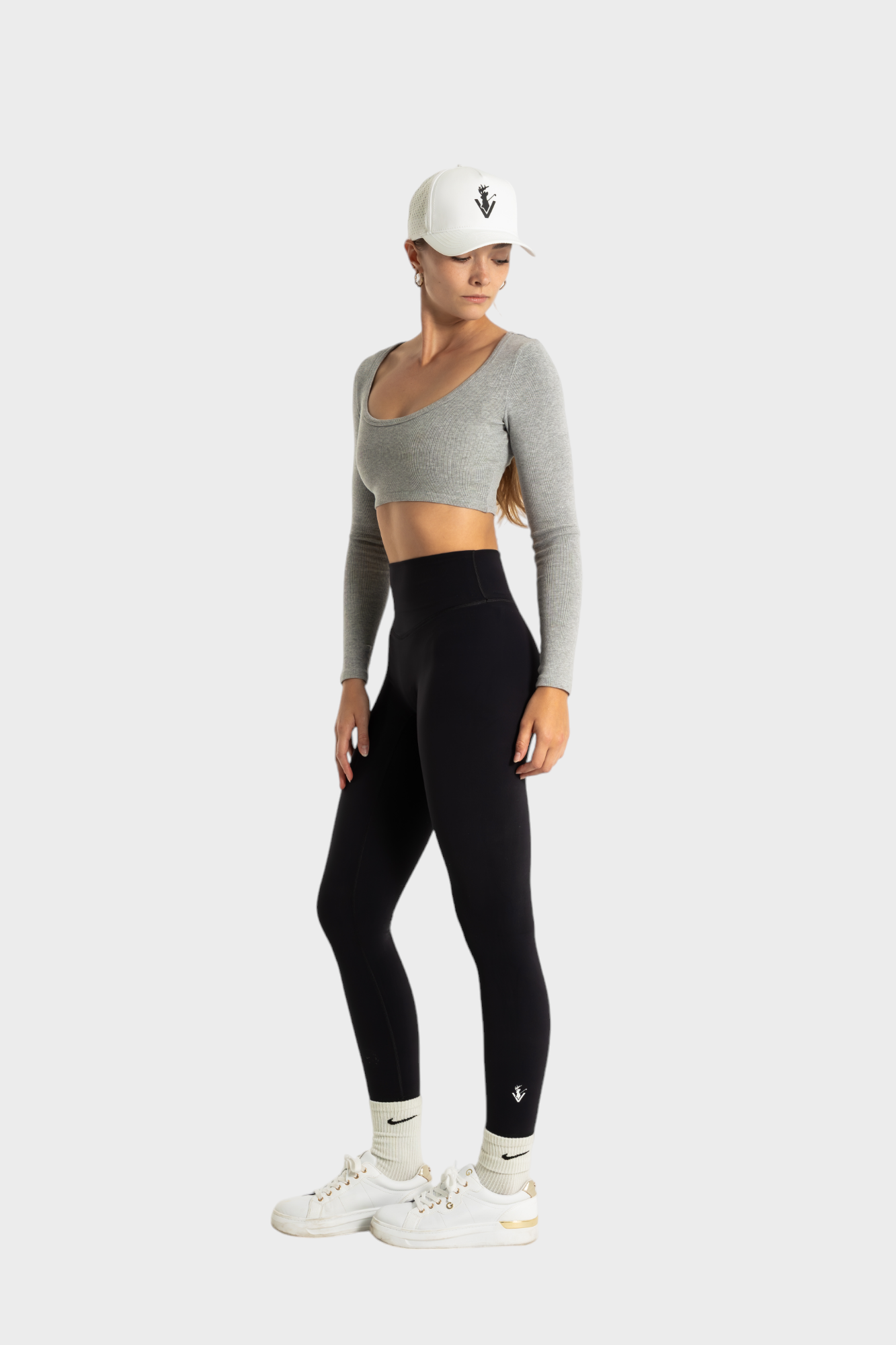Woman wearing black Sollevare leggings and gray crop top with white cap and sneakers against white background