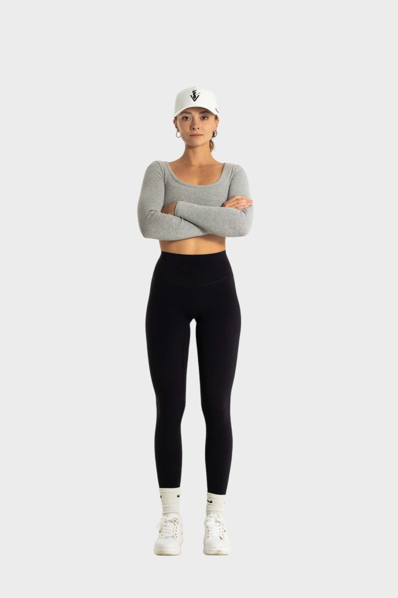 Woman wearing black Sollevare leggings by VittoriaGolfCo with gray long sleeve crop top and white cap against white background