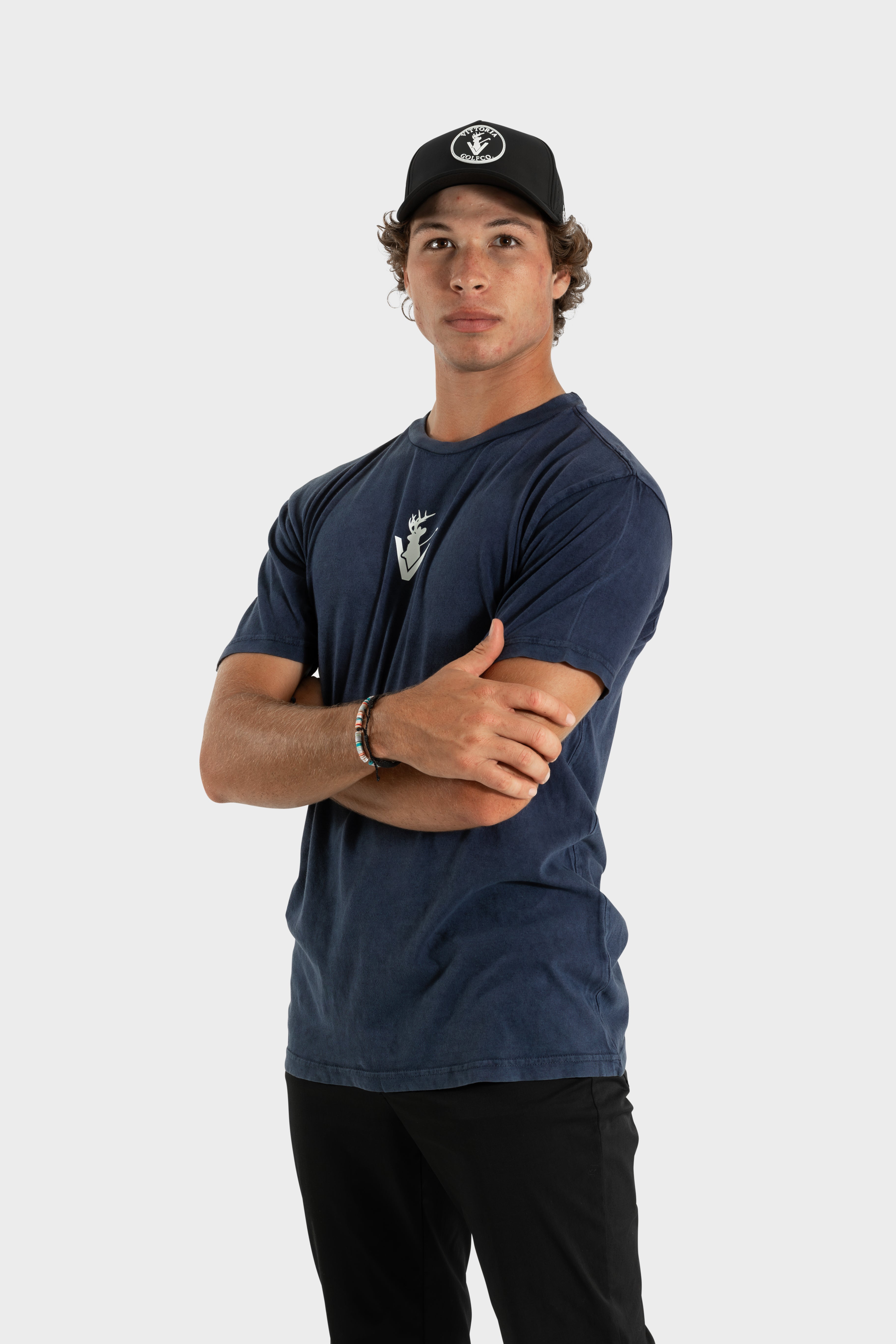 Man wearing navy Vittoria Oversized Tee with logo and black cap against white background