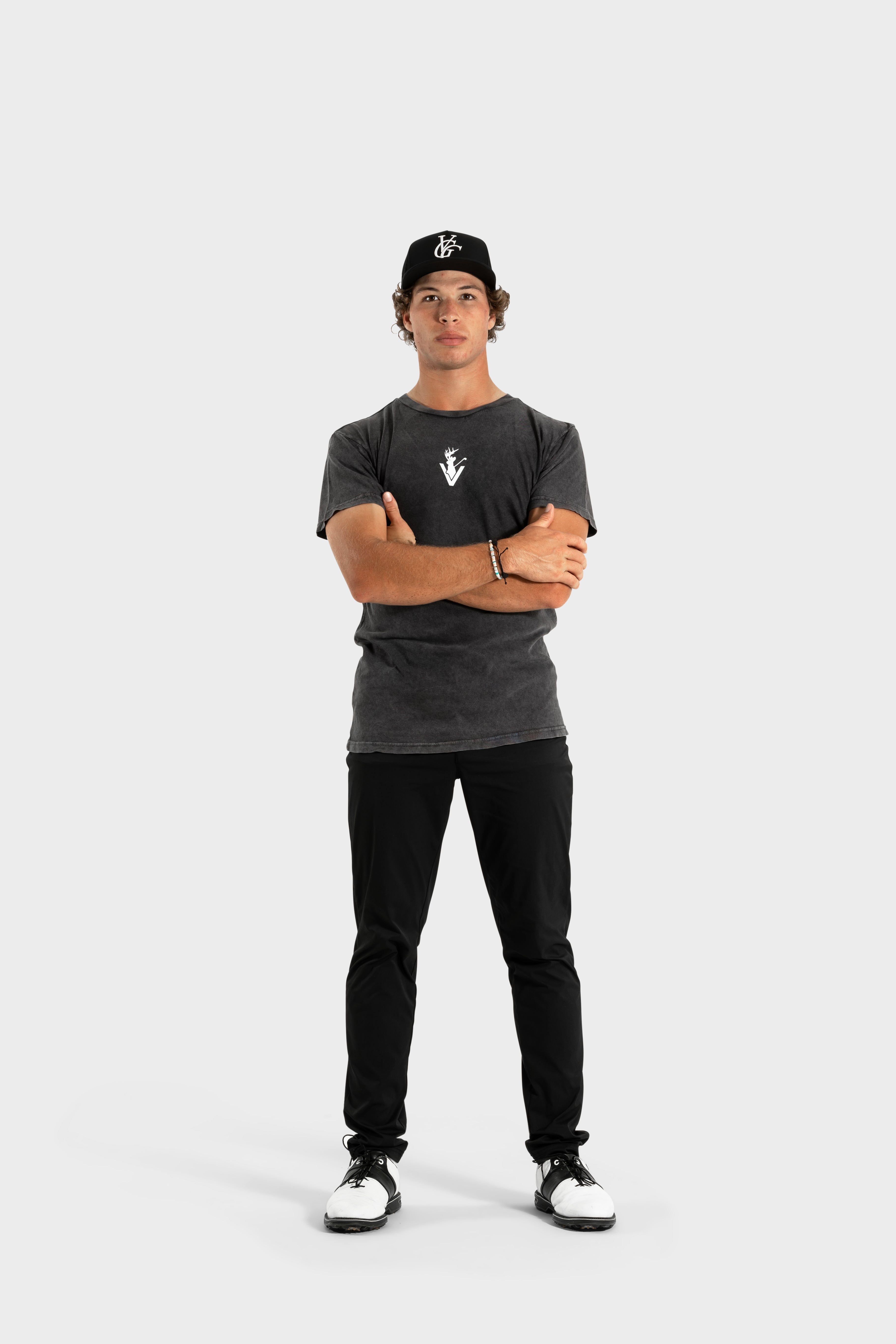 Man wearing black Vittoria Oversized Tee with logo, black pants, and cap standing against white background