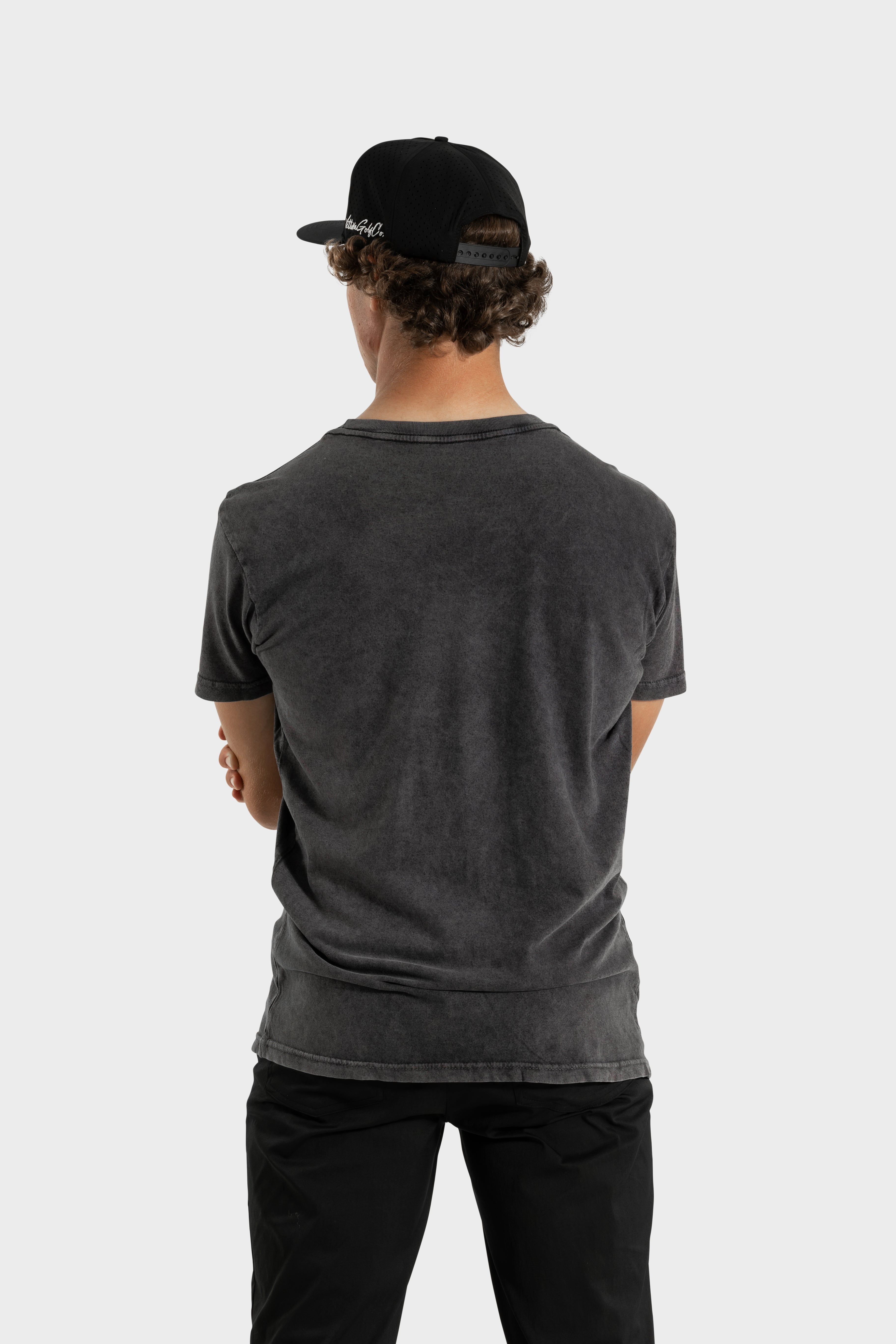 Back view of man wearing black Vittoria Oversized Tee and black cap against white background