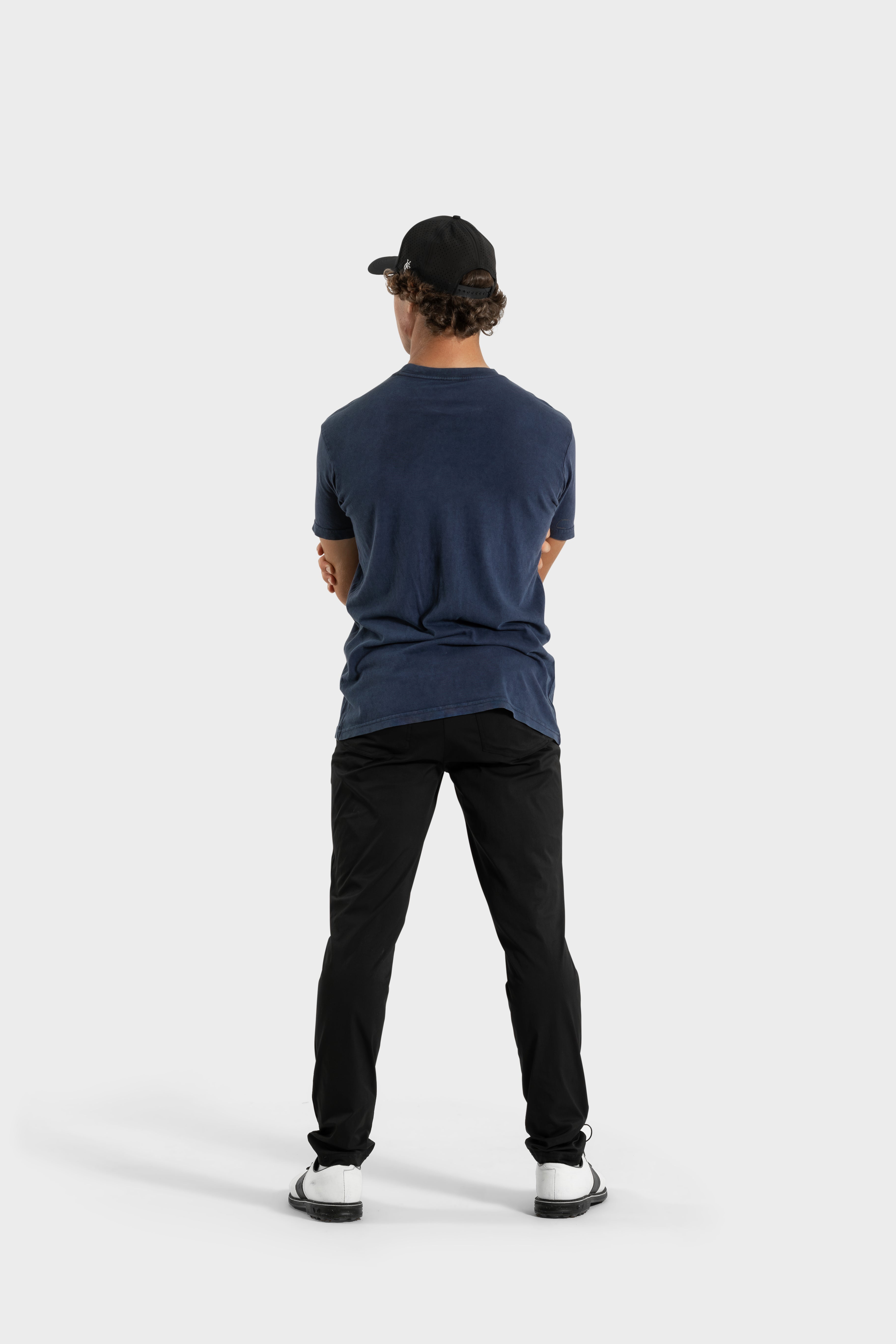 Man wearing navy Vittoria Oversized Tee with black pants and cap facing away on white background