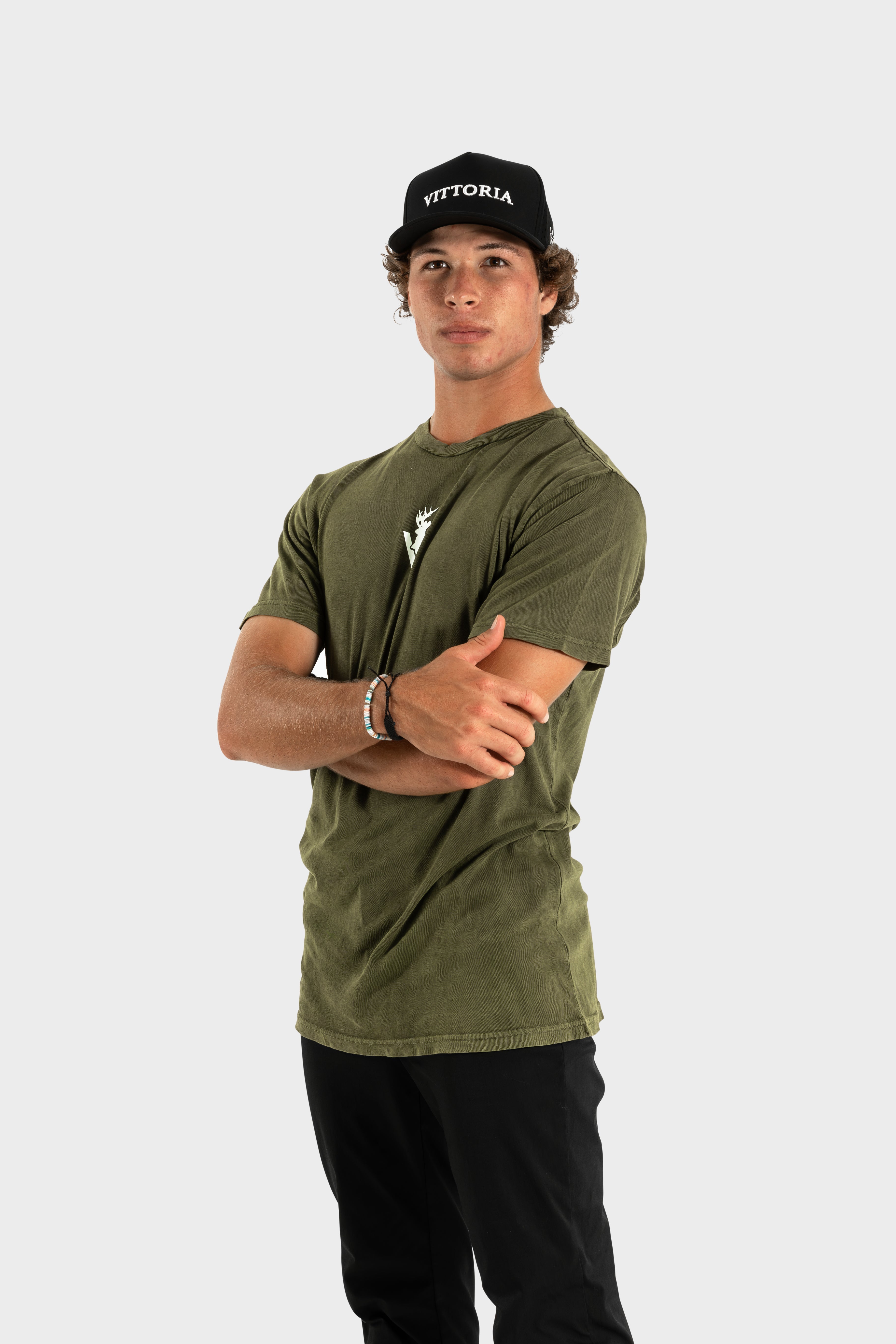 Man wearing olive green Vittoria Oversized Tee with Vittoria cap and black pants against white background