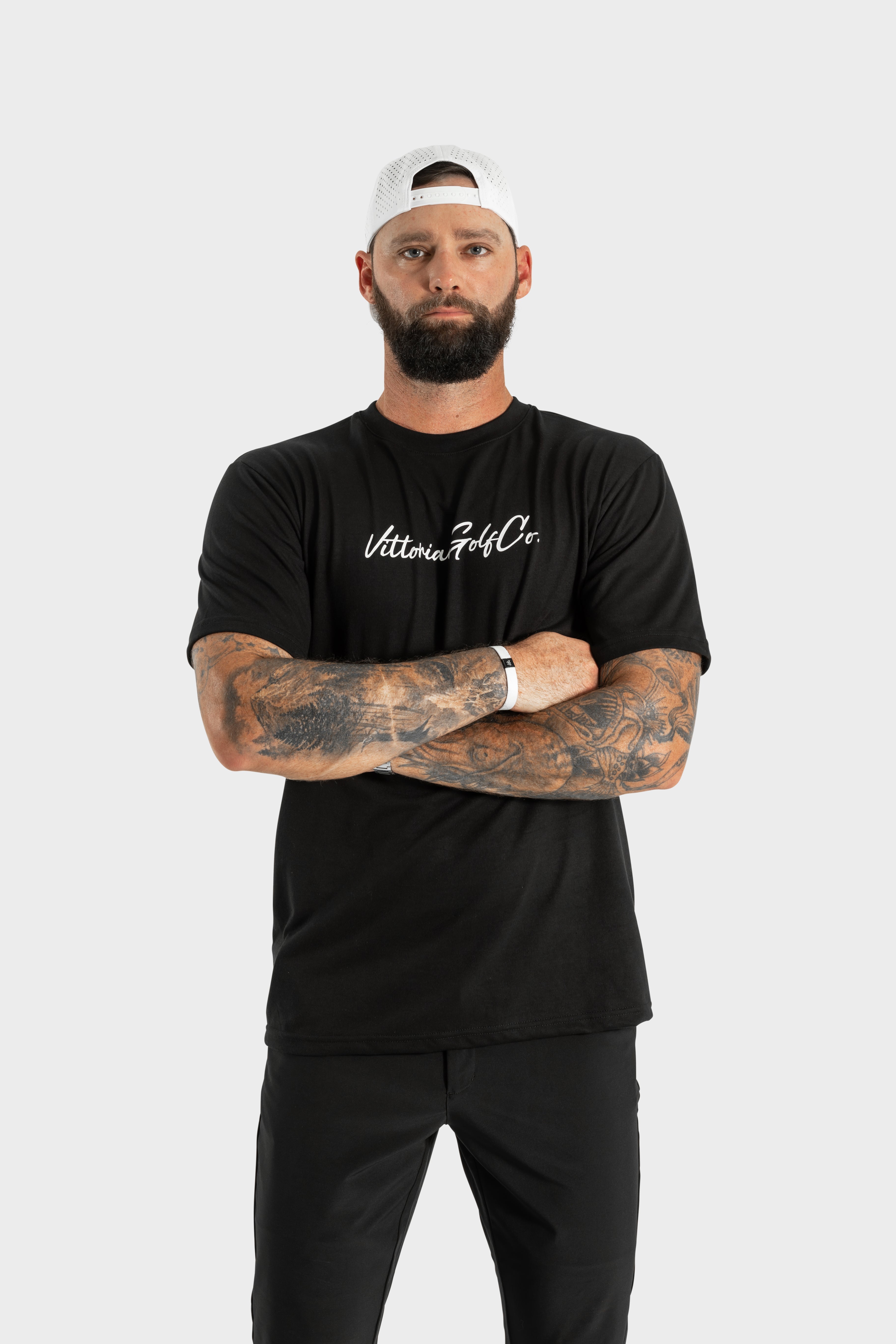 Man wearing black Vittoria Basic Tee with Vittoria Golf Co. logo and white cap