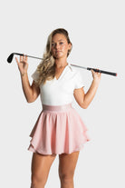 Woman wearing light pink Blossom golf skirt holding golf club over shoulders standing against white background