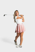 Woman in white top and pink Blossom golf skirt swinging golf club on white background