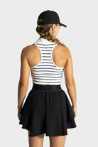 Woman wearing Blossom golf skirt in black with striped sleeveless top and black cap viewed from back