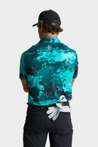 Back view of man wearing The One polo by VittoriaGolfco in teal camo pattern with black cap and golf glove tucked in pants