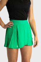 Woman wearing green Perfetta golf skirt with pleated design and built-in shorts, paired with black sleeveless top
