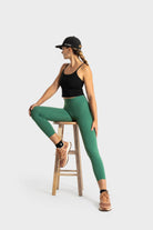 Woman wearing green The Quelles leggings by VittoriaGolfCo sitting on a wooden stool in a black tank top and sports shoes